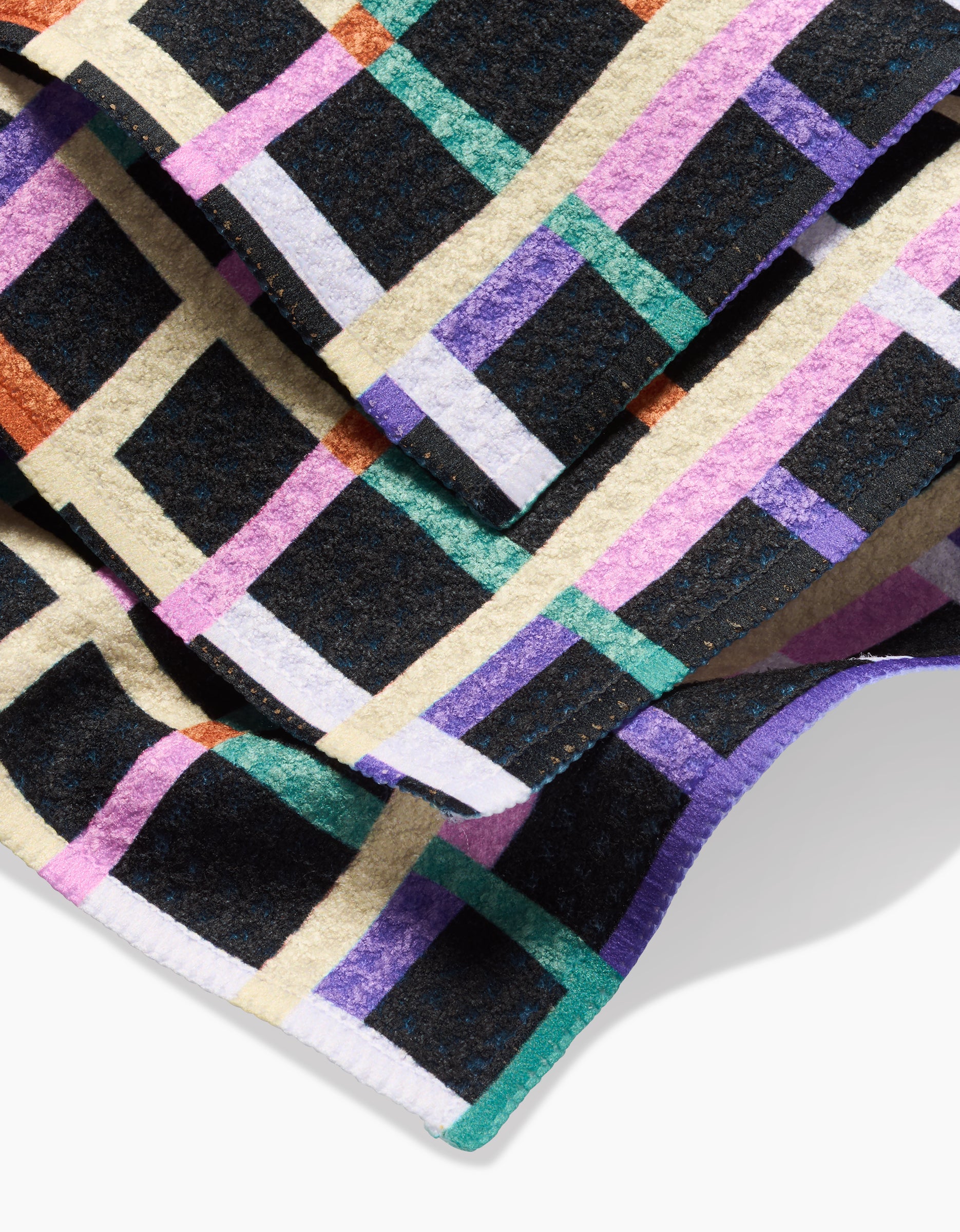 A close-up of the Claire Iglesias Happy Plaid Geoweave dishcloth, showcasing its colorful geometric plaid pattern with purple, green, orange, cream, and black lines.