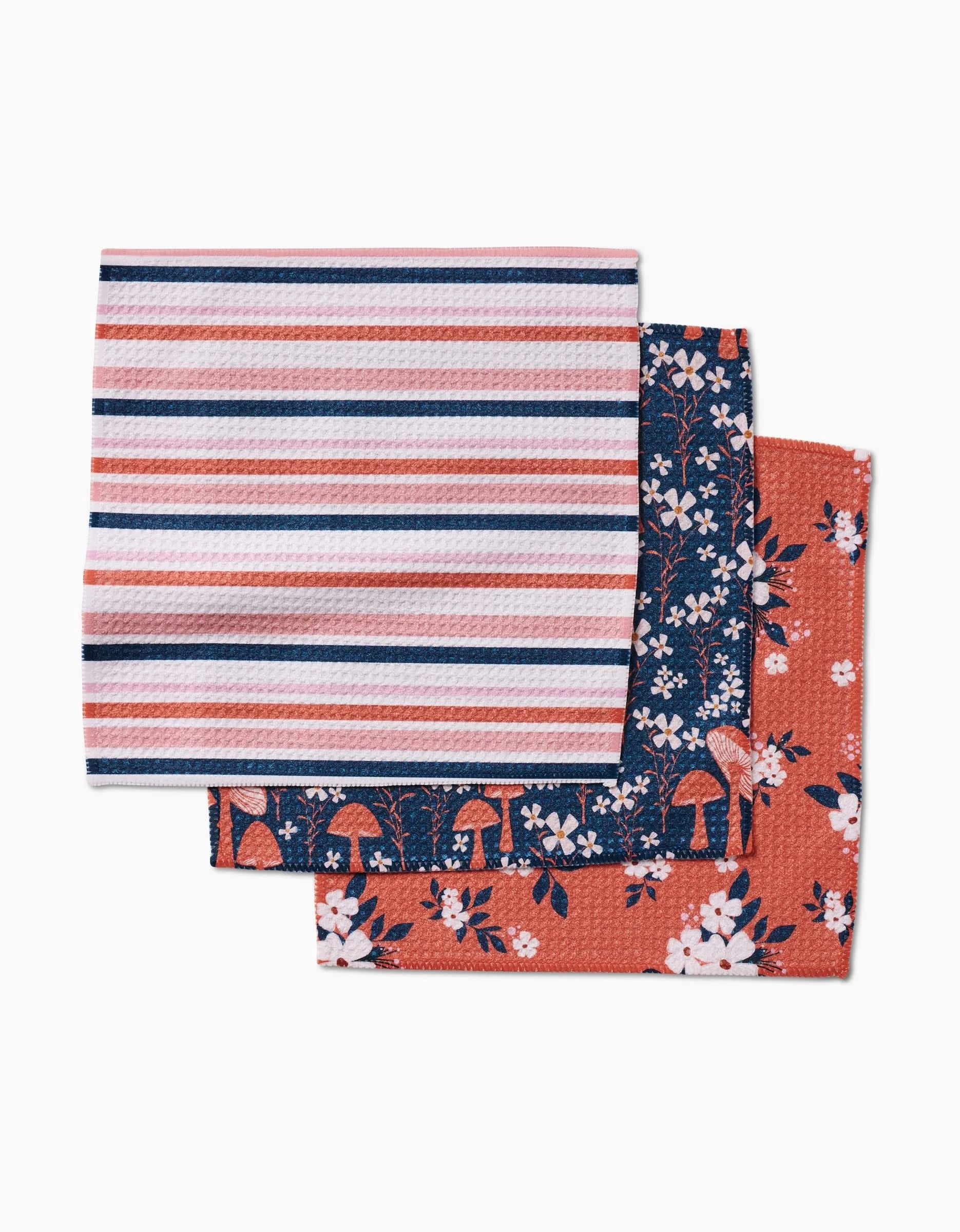 The Harvest Season dish towel set by Charlie Rowan Designs includes three Geoweave towels: pink/white/blue stripes, blue with white mushrooms, and reddish with white florals and mushrooms.