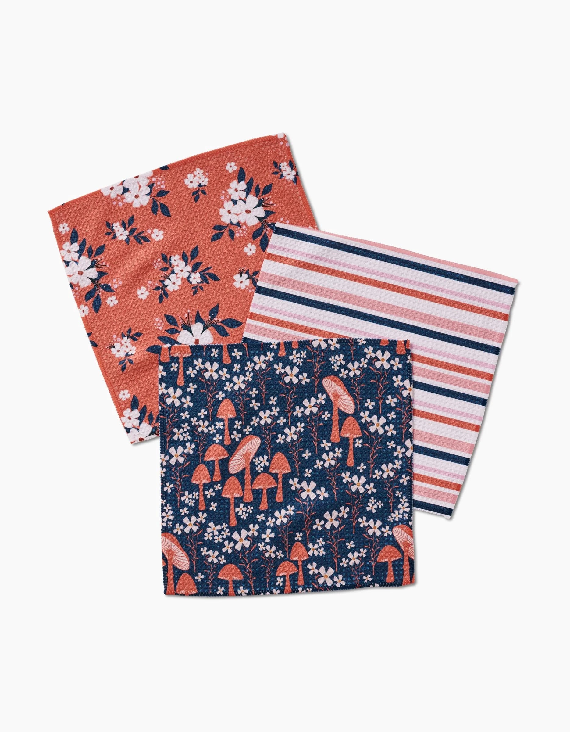 The Harvest Season dishcloth set by Charlie Rowan Designs features three designs: white and pink flowers on red, pink/navy/white stripes, and red mushrooms with flowers on navy geoweave made from recycled materials.