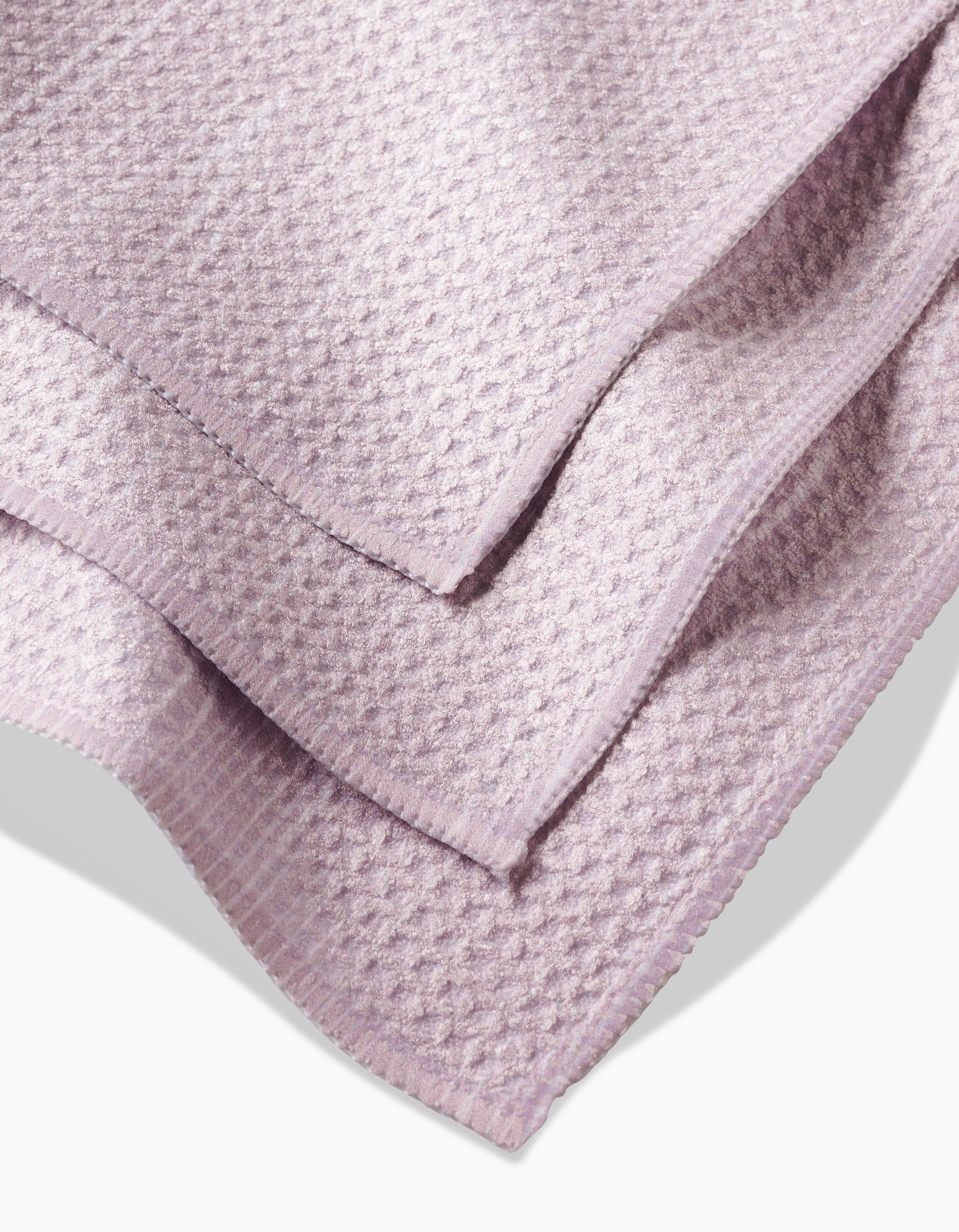 A close-up view of folded Houston Wood dishcloth by Kailee Wright features textured, waffle-like Geoweave fabric in light lavender with neatly finished edges.