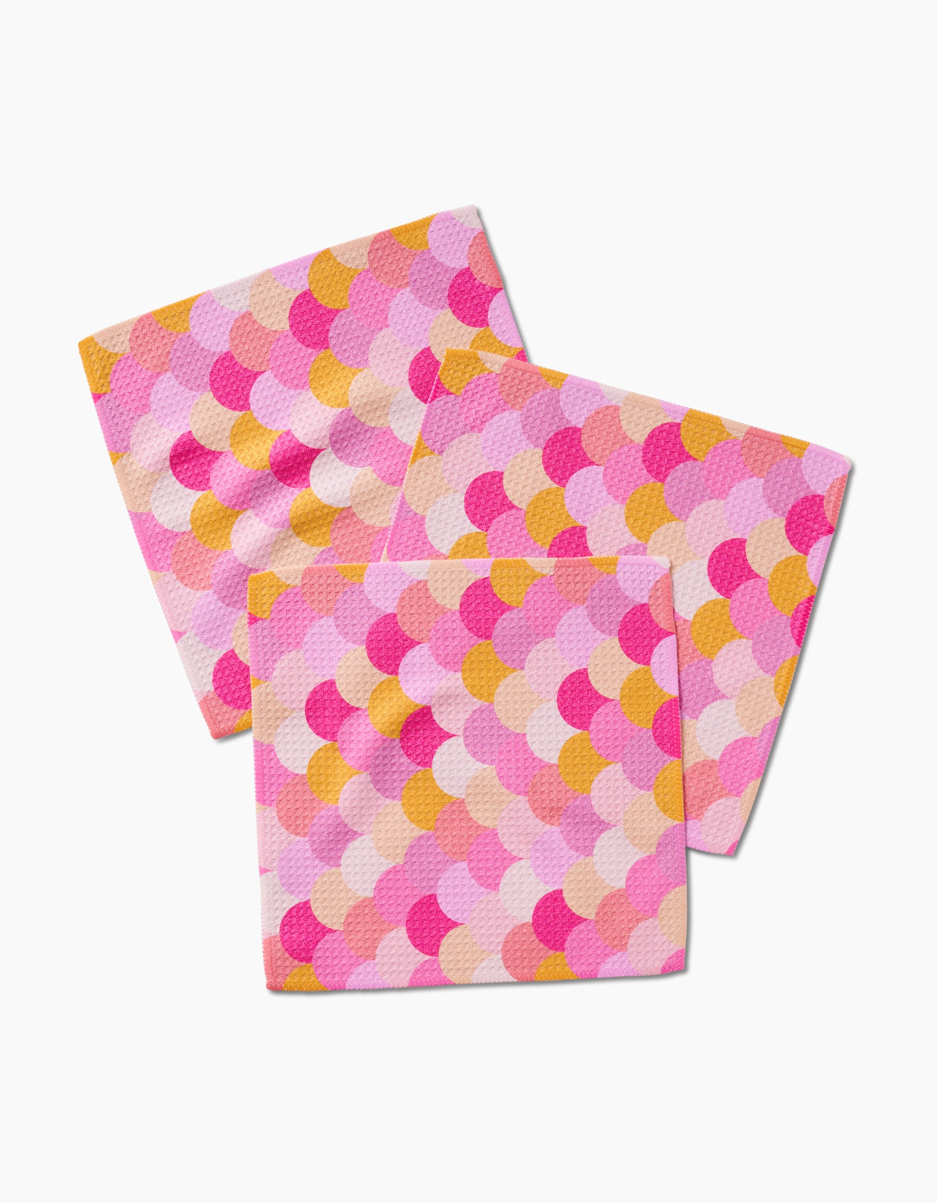 Three GEOMETRY Inherit dishcloths made from recycled materials, featuring a pink, orange, and yellow scallop pattern, are overlapped on a white background.