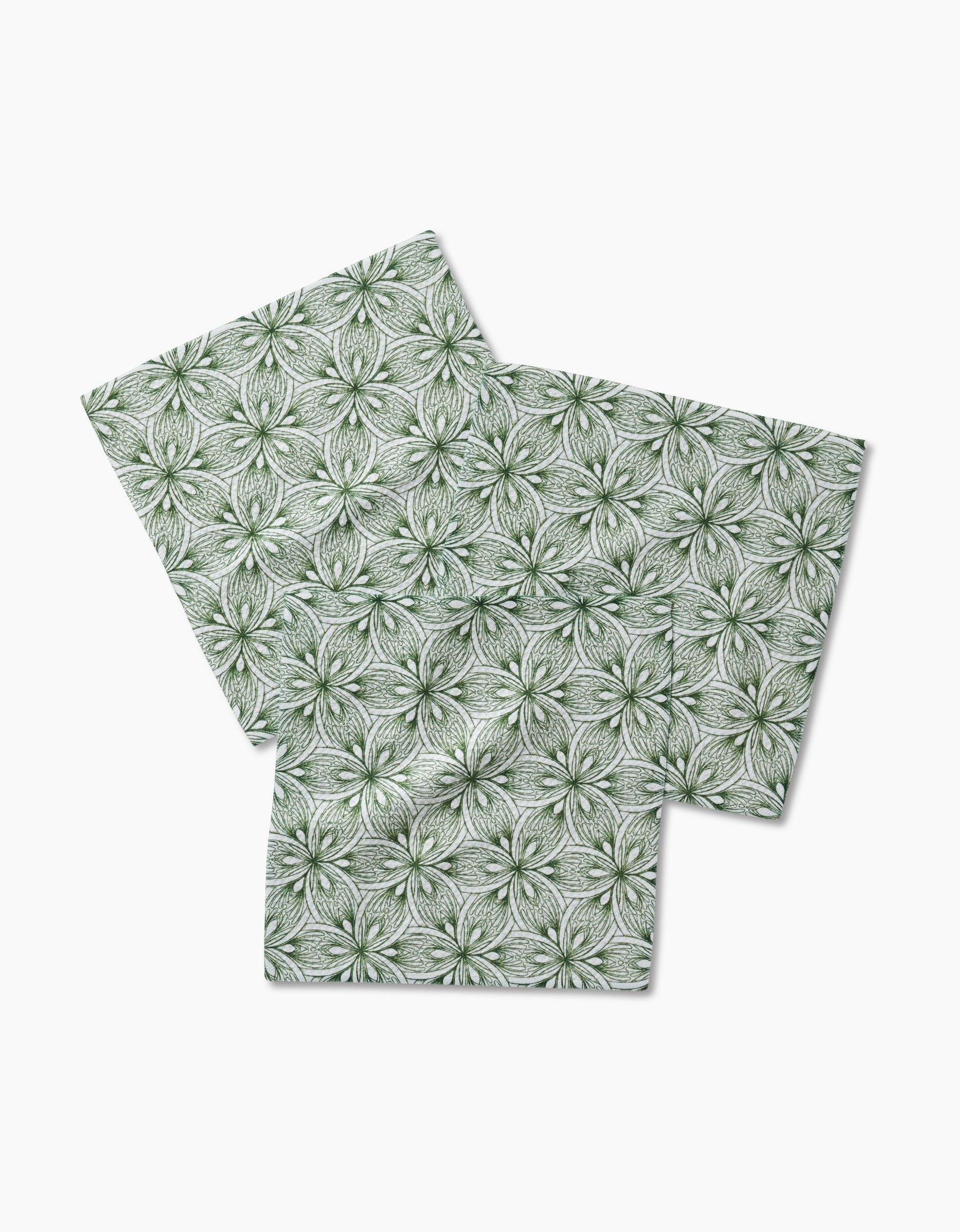Three Interlaced Petals square paper napkins by Marta Harvey, featuring a green and white symmetrical floral pattern and made from recycled materials, arranged overlapping on a white background.