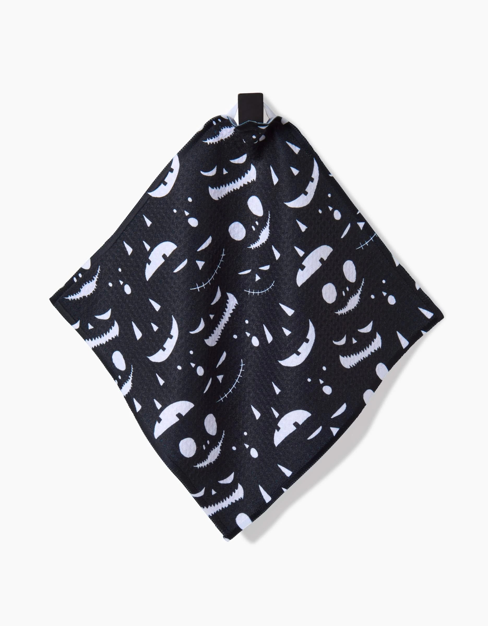 The Jack O Lantern Jamboree napkin by Danelys Sidron features white Halloween faces on black recycled cloth and a corner loop for hanging.