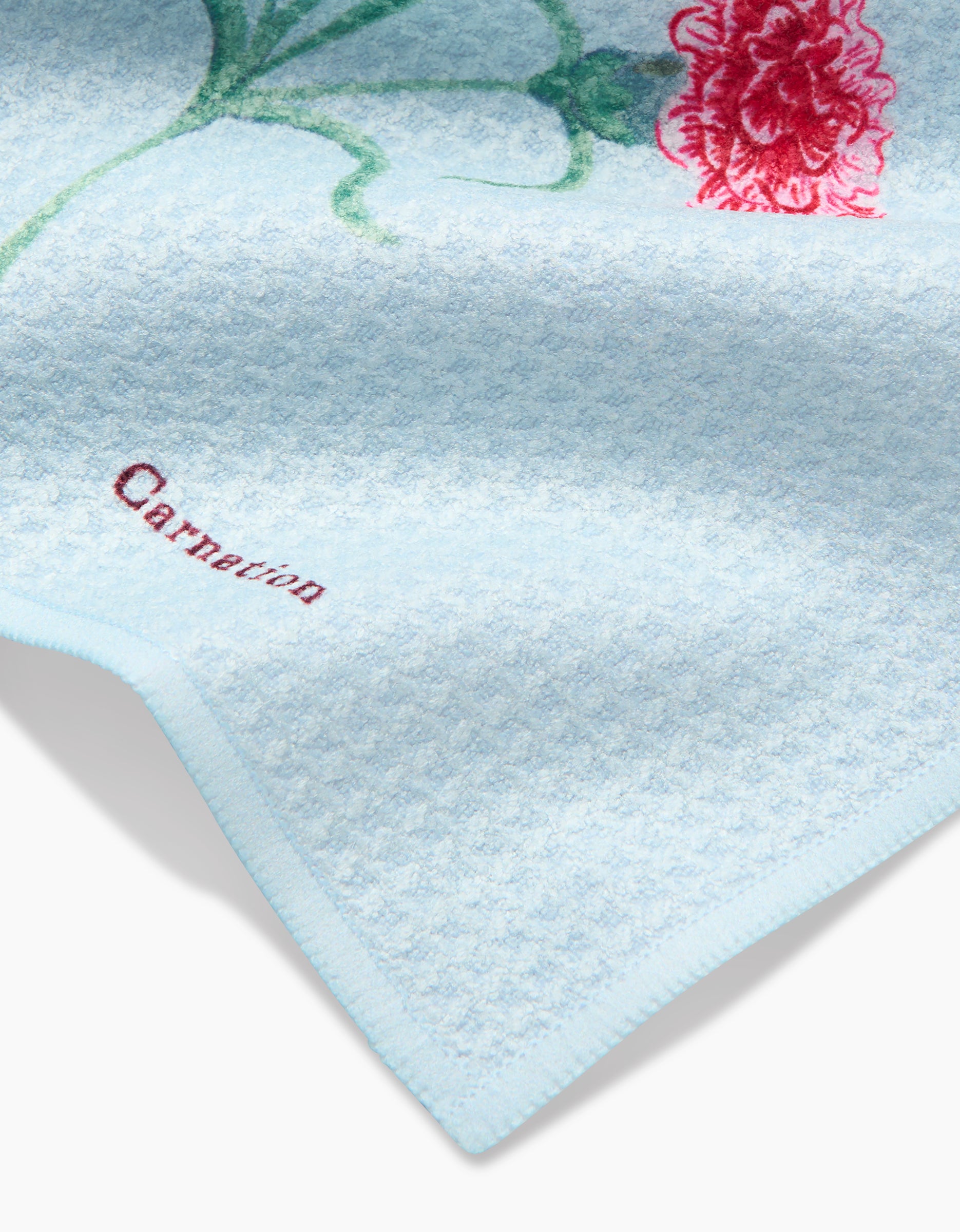 The Linda Fox January Carnation towel features light blue Geoweave fabric, an embroidered red carnation and green stem, plus Carnation stitched in red near the edge—combining style and absorbency in one charming dishtowel.
