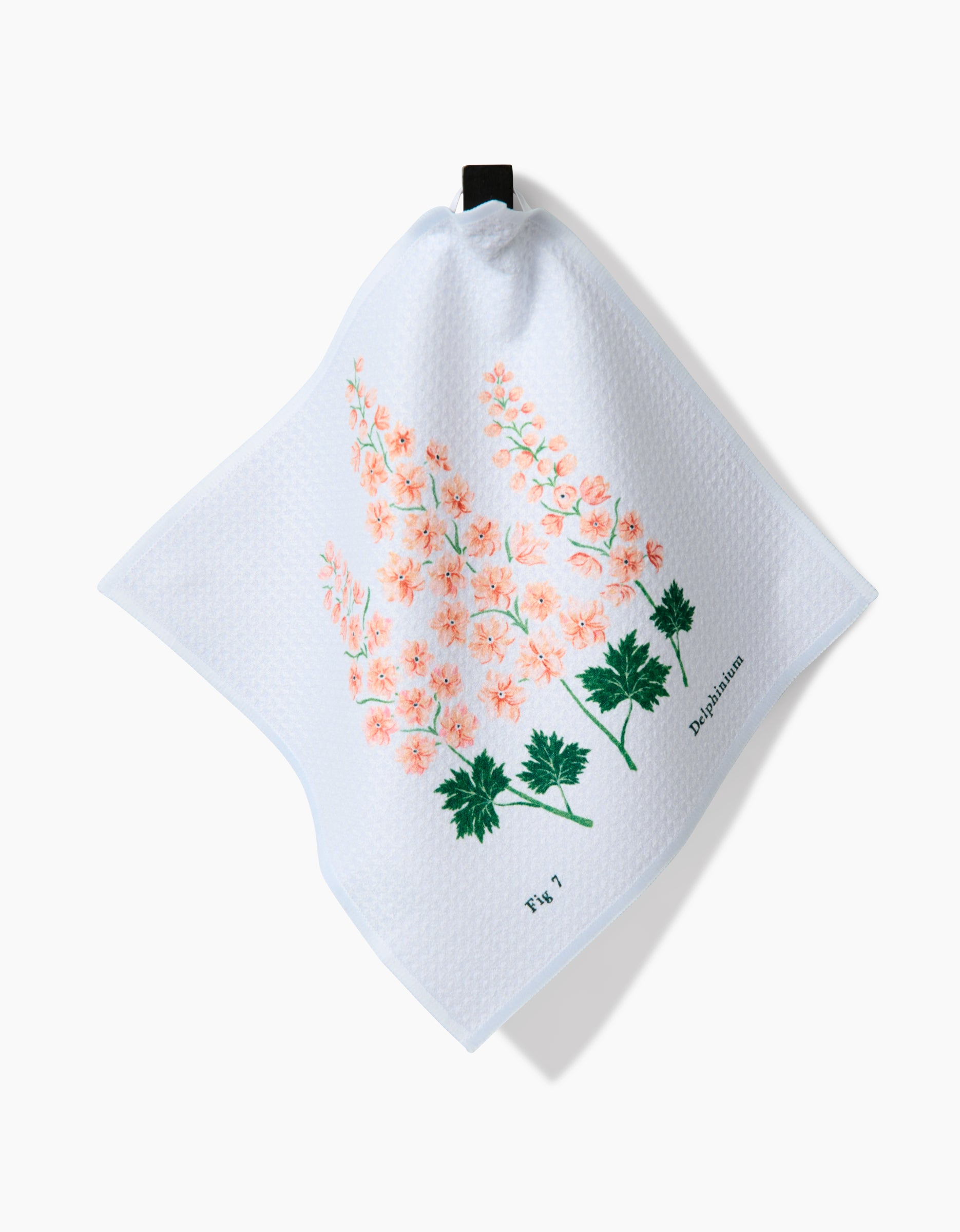 The Linda Fox July Delphinium dishcloth is white and textured, made from recycled materials, with pink and green botanical artwork labeled Delphinium and Fig 7, and features a black hanging loop.