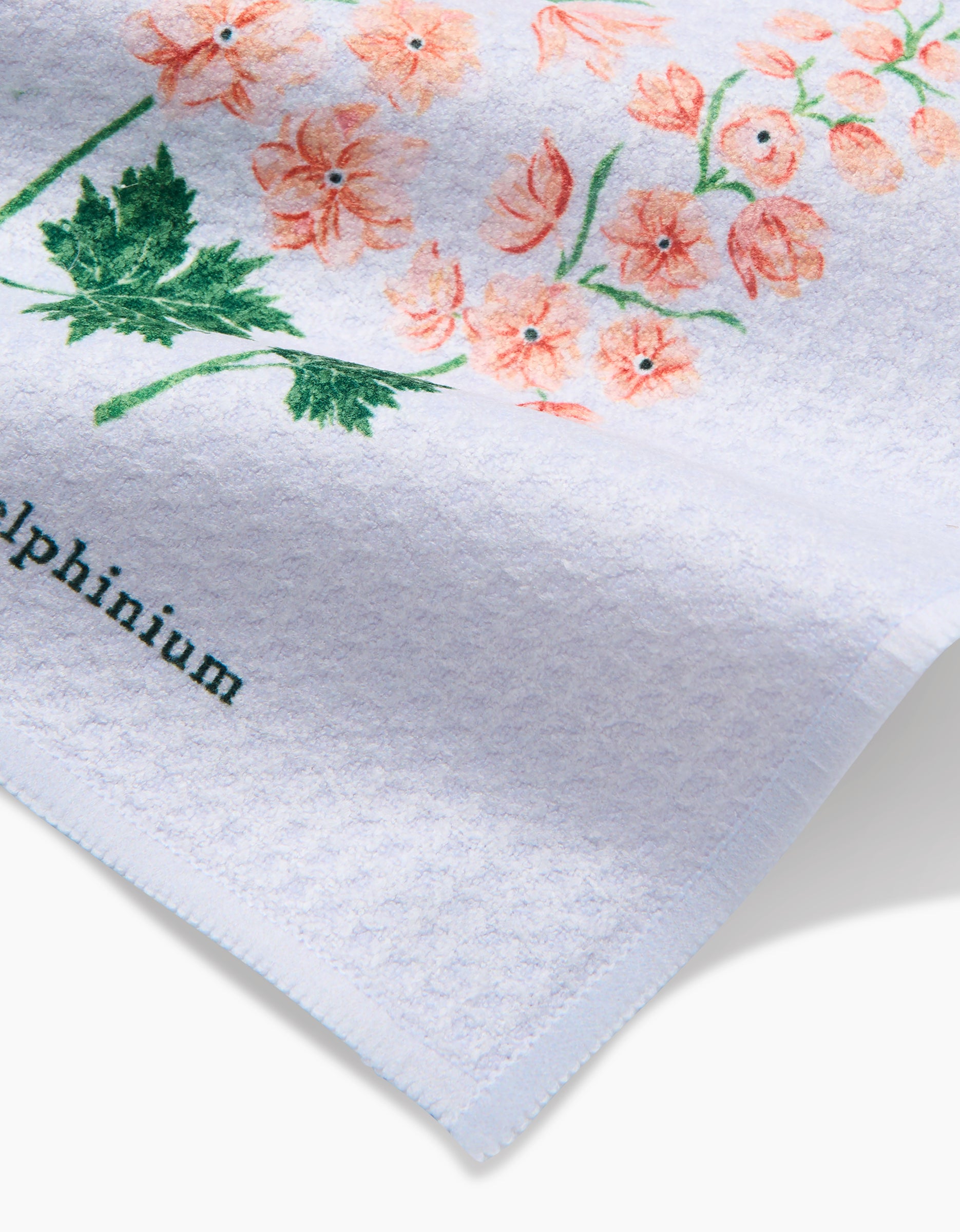The July Delphinium dishcloth by Linda Fox is a white textured cloth made from recycled materials, featuring pink flowers with green stems and Delphinium partly visible in black at the bottom left.