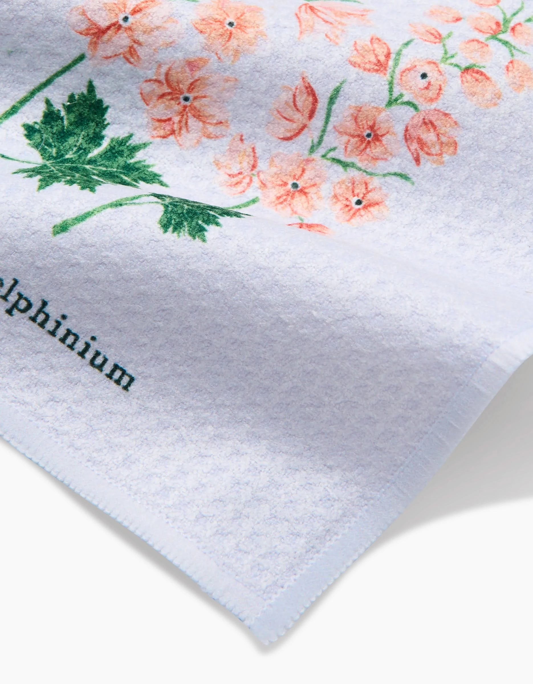 The July Delphinium dishcloth by Linda Fox is a white textured cloth made from recycled materials, featuring pink flowers with green stems and Delphinium partly visible in black at the bottom left.