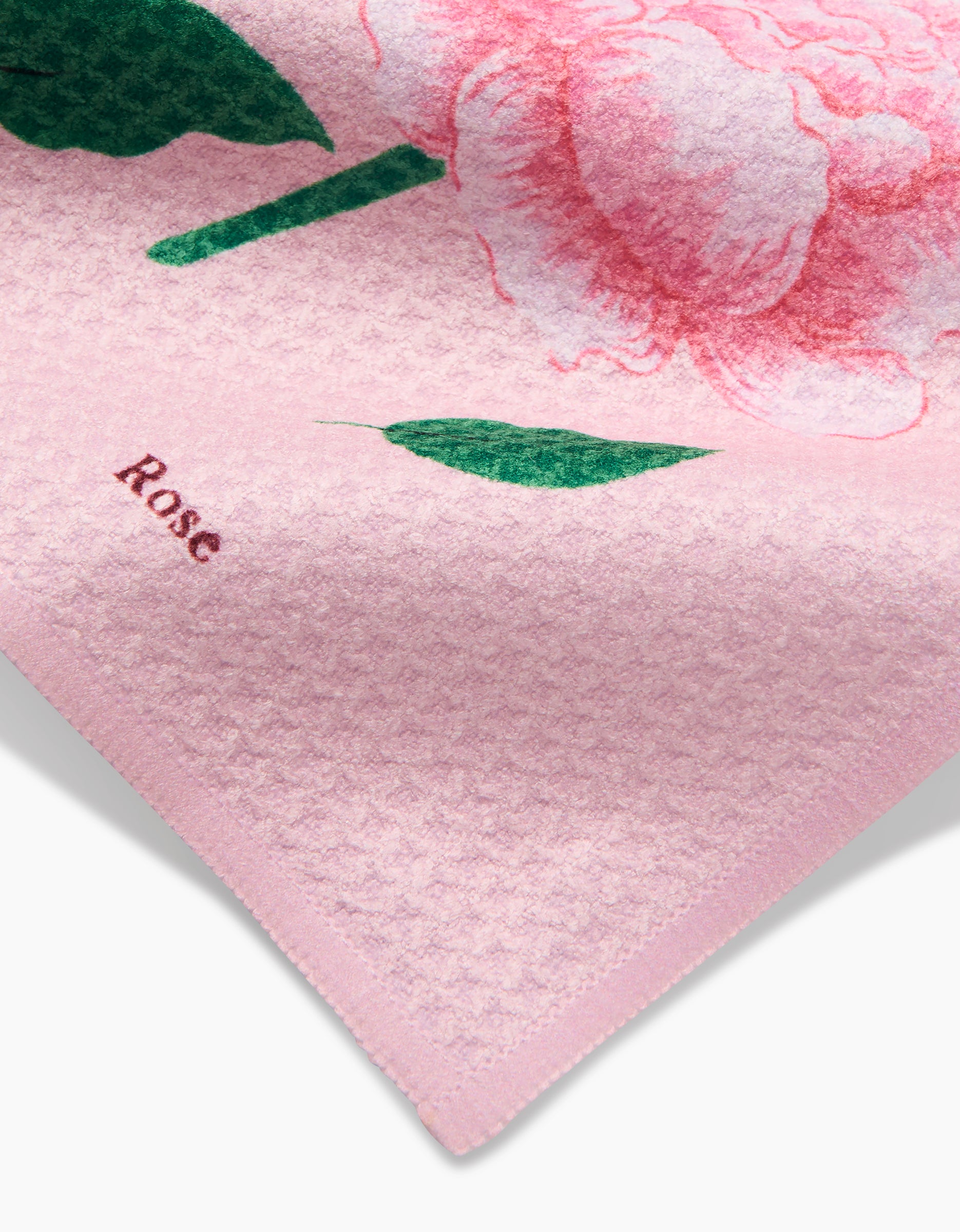 A close-up of the June Roses dishcloth by Linda Fox, crafted from recycled materials, shows a large pink flower with green leaves and Rose in red near the corner.