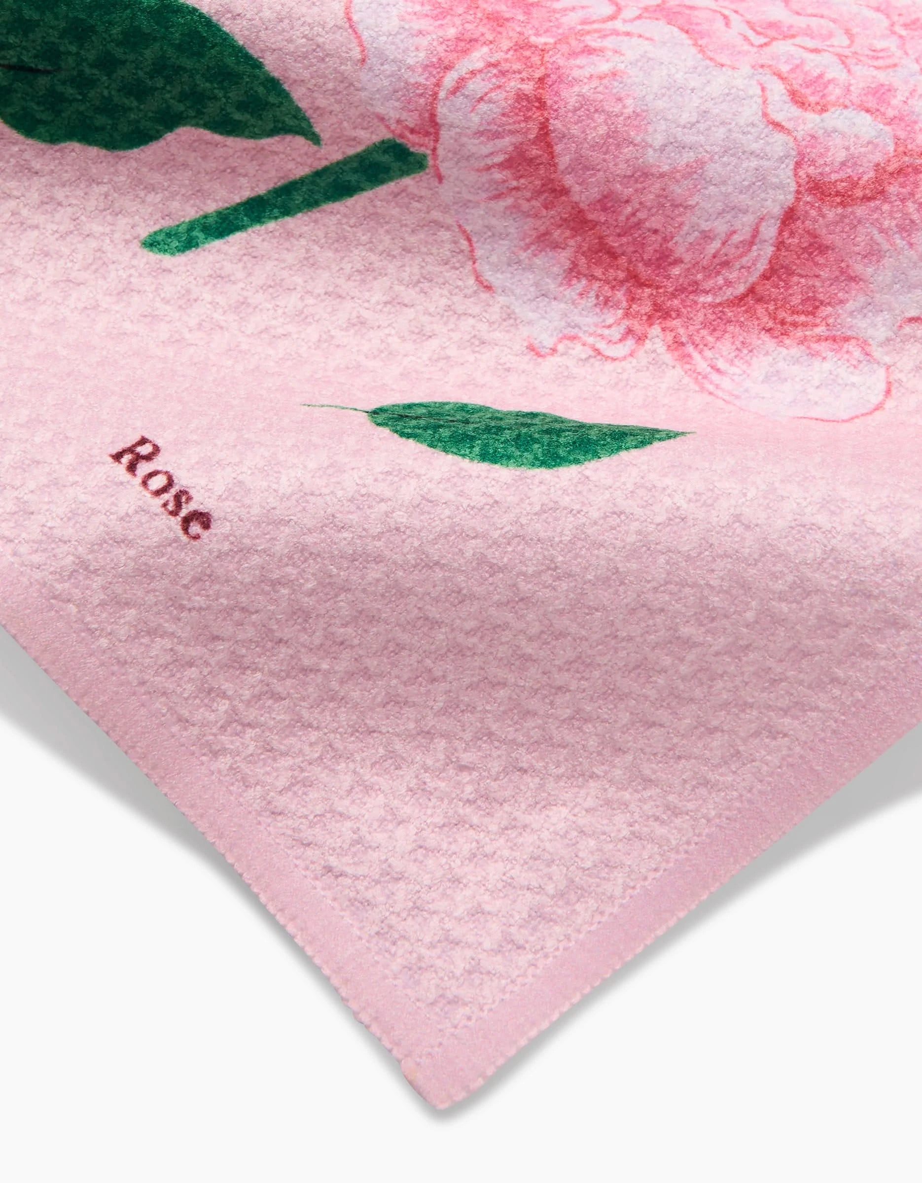 A close-up of the June Roses dishcloth by Linda Fox, crafted from recycled materials, shows a large pink flower with green leaves and Rose in red near the corner.
