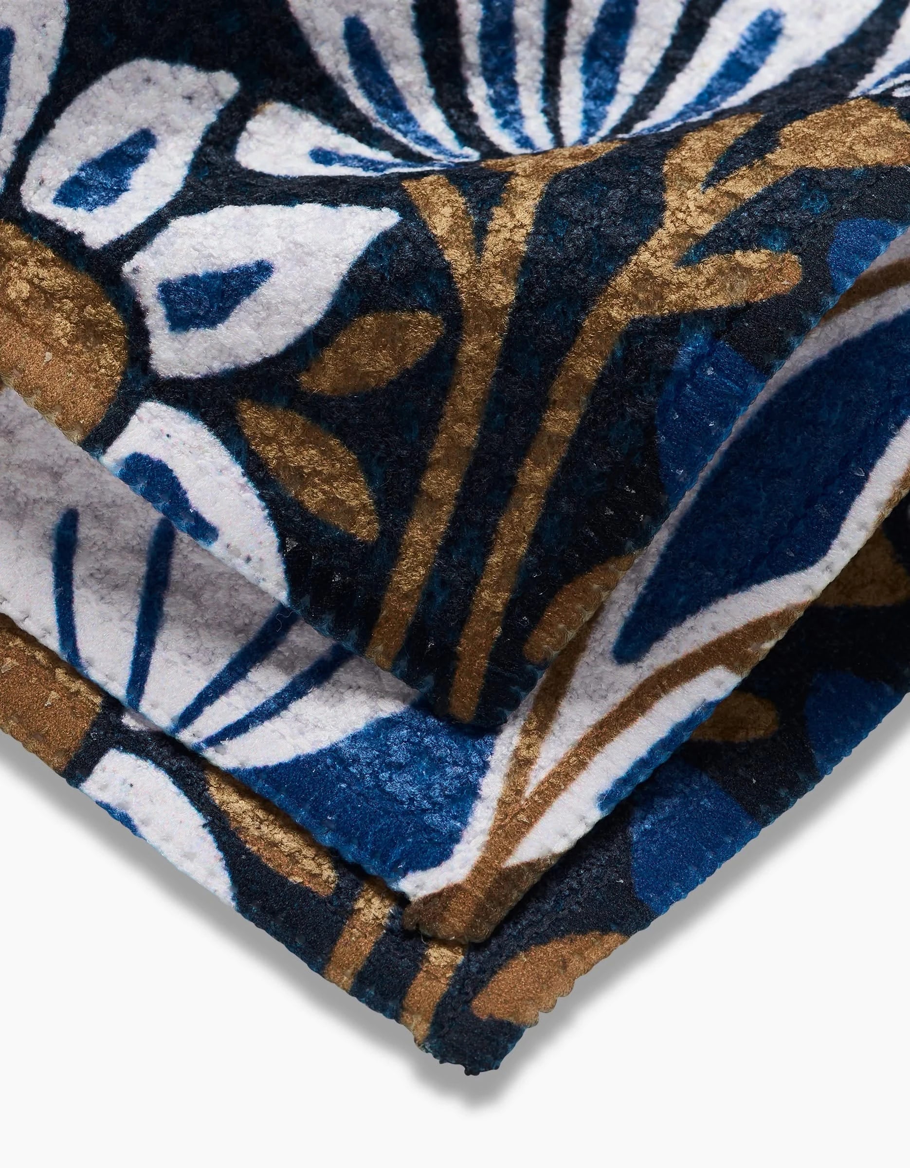 A close-up of Leslie Flowers fabric by Amy MacCready shows bold, textured floral and leaf patterns in white, blue, brown, and black. Made from recycled materials, it features large stylized designs.