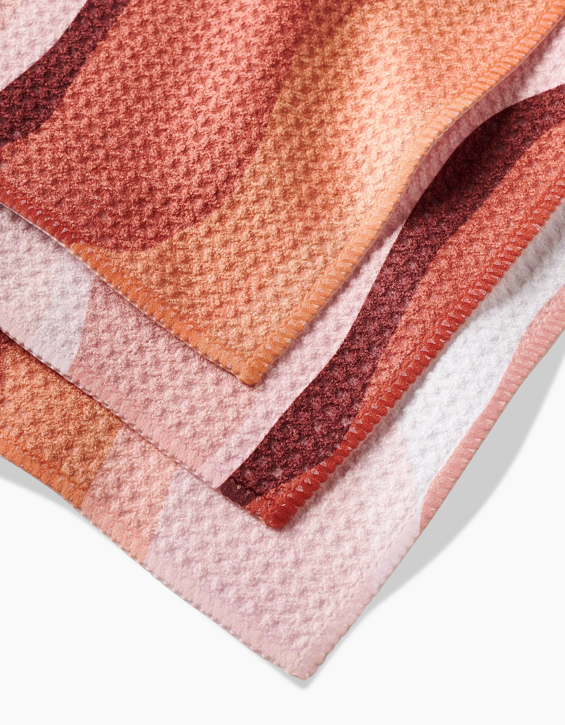 Close-up of two overlapping GEOMETRY Levels of Fall towels, made from Geoweave™ fabric with a textured waffle-like weave and abstract pink, peach, and red patterns—ideal as a super-absorbent dishcloth.