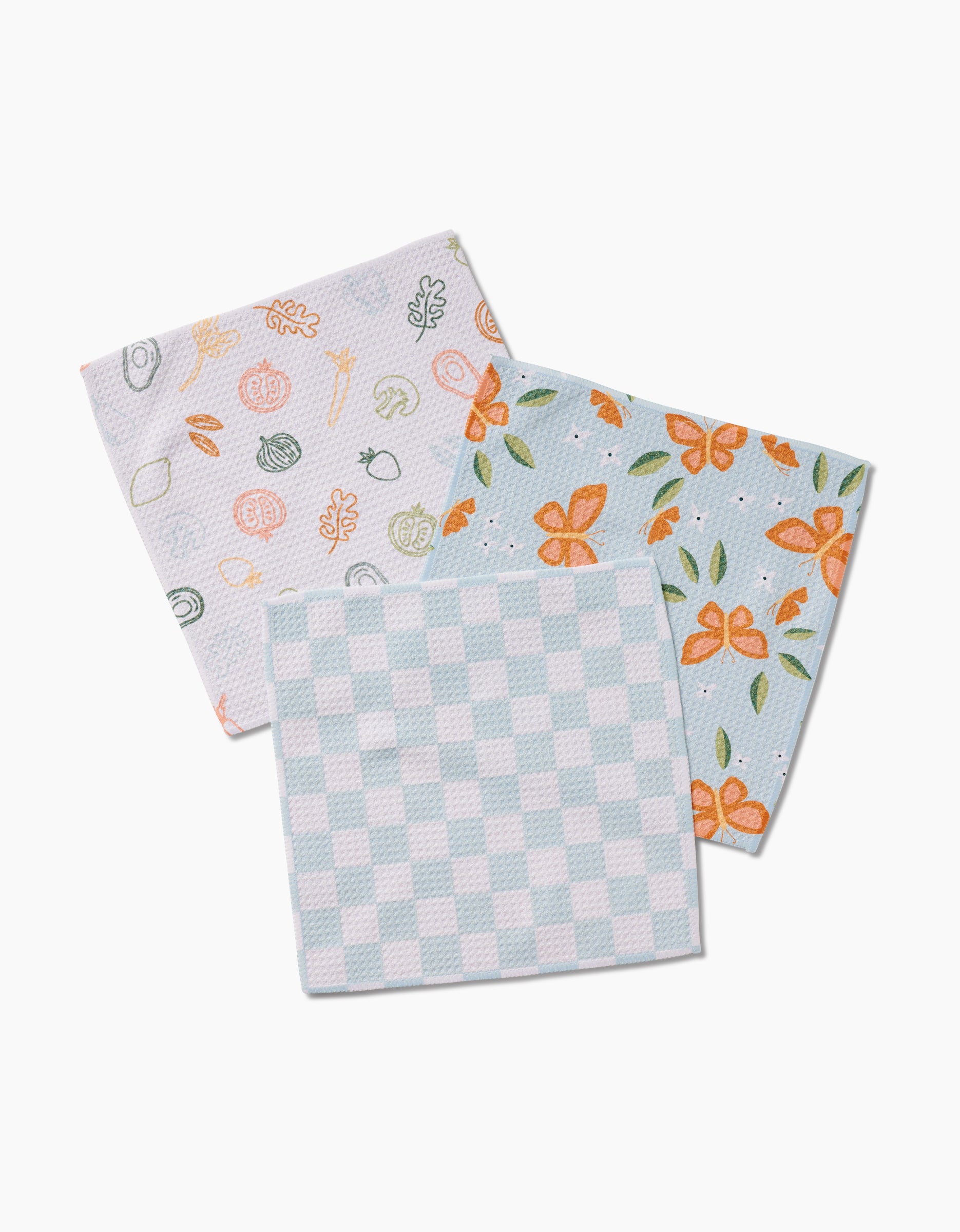Three folded Life is Beautiful dishcloths by Sweet Simple Vegan overlap on a white surface: one has a pastel sushi pattern, one features orange flowers with green leaves on blue, and one displays a light blue and white checkered design.