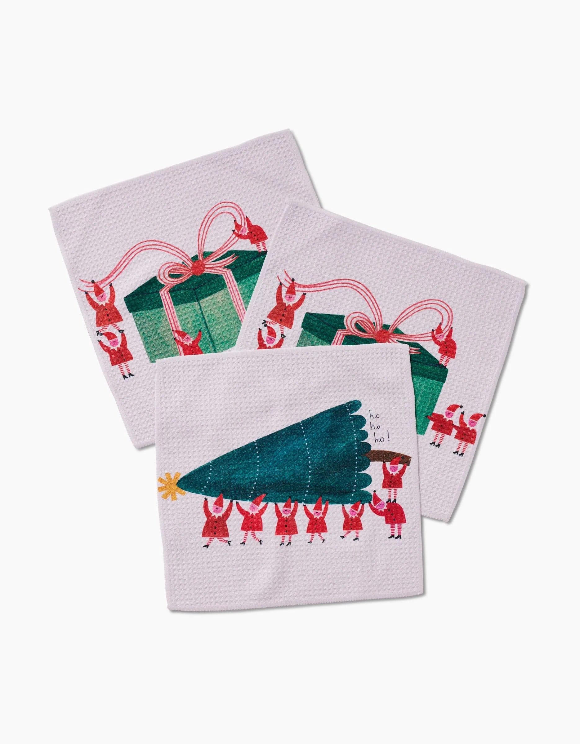 The Little Helpers set by Daria Solak includes three white Geoweave dishcloths: two feature red-outfitted figures holding a big green gift with a pink ribbon, and one shows them carrying a Christmas tree labeled “ho ho ho!”.