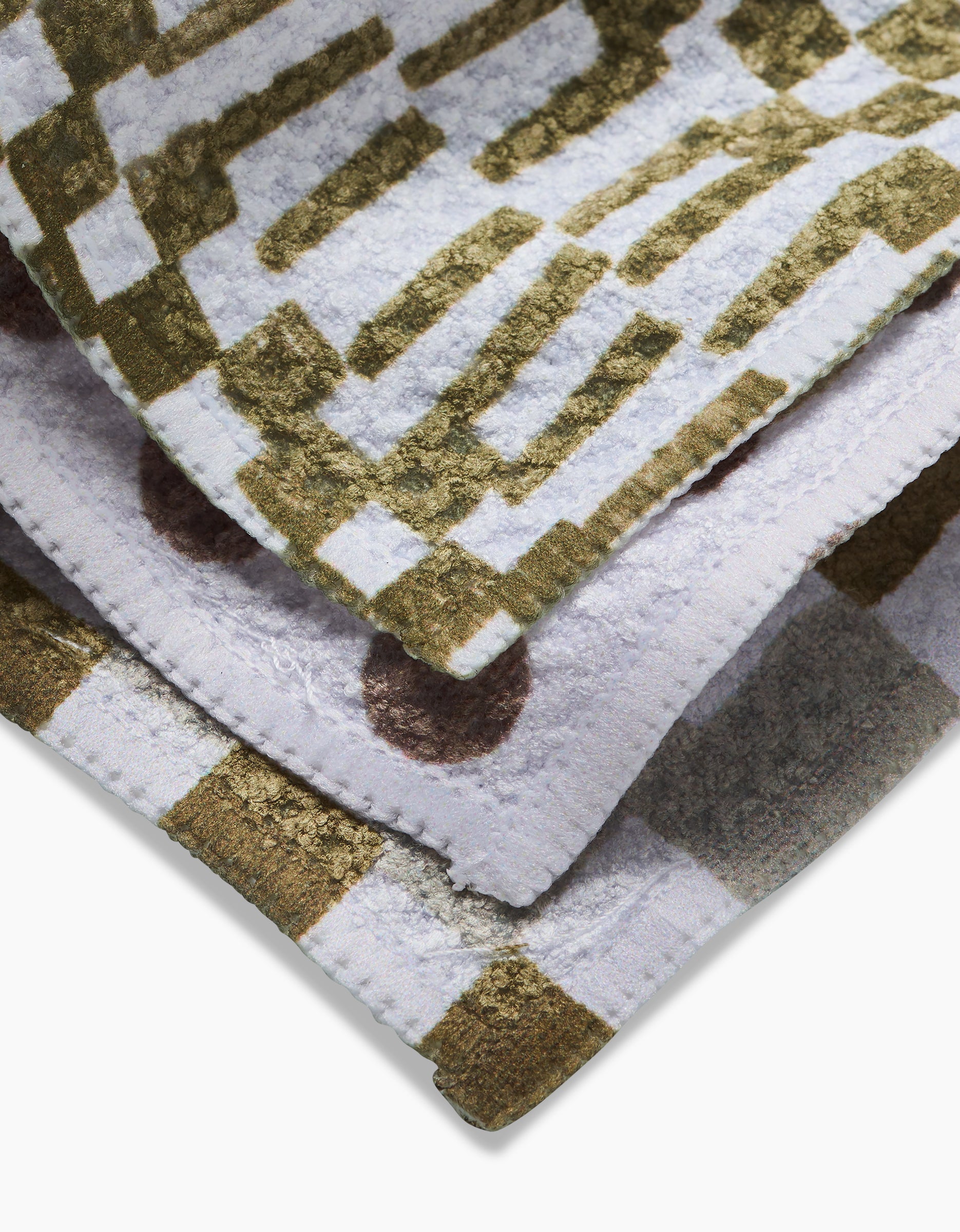 The Lotty towels by Studio Jeannot are crafted from soft Geoweave fabric with abstract gold, brown, and white patterns. Featuring stripes, dots, and grids, these plush towels are made using recycled materials.
