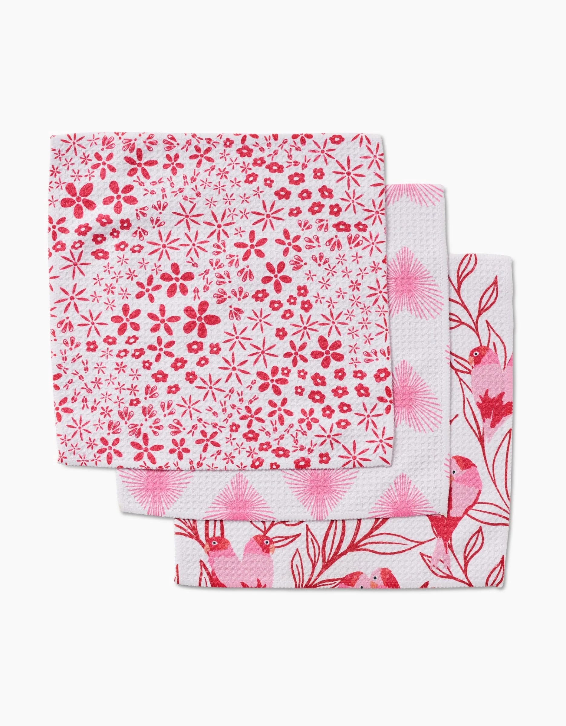 Three folded Hufton Studio Love Birds dishcloths, each with unique pink and red patterns—flowers, dots, birds, and branches—made from recycled materials.