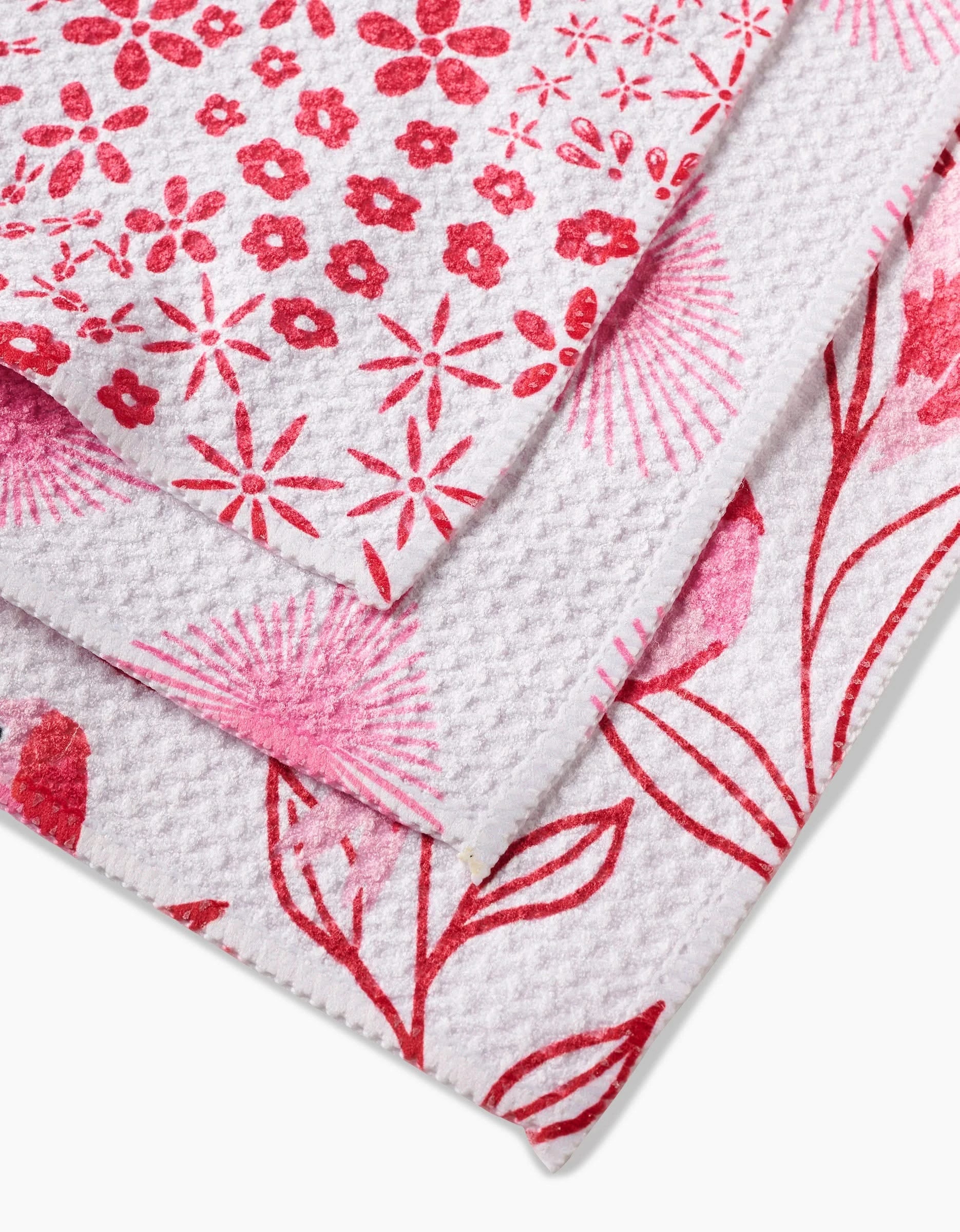 Three overlapping Hufton Studio Love Birds dishcloths, made from durable Geoweave fabric with red floral and leaf patterns, feature textured surfaces and neat edges, arranged diagonally against a plain background.