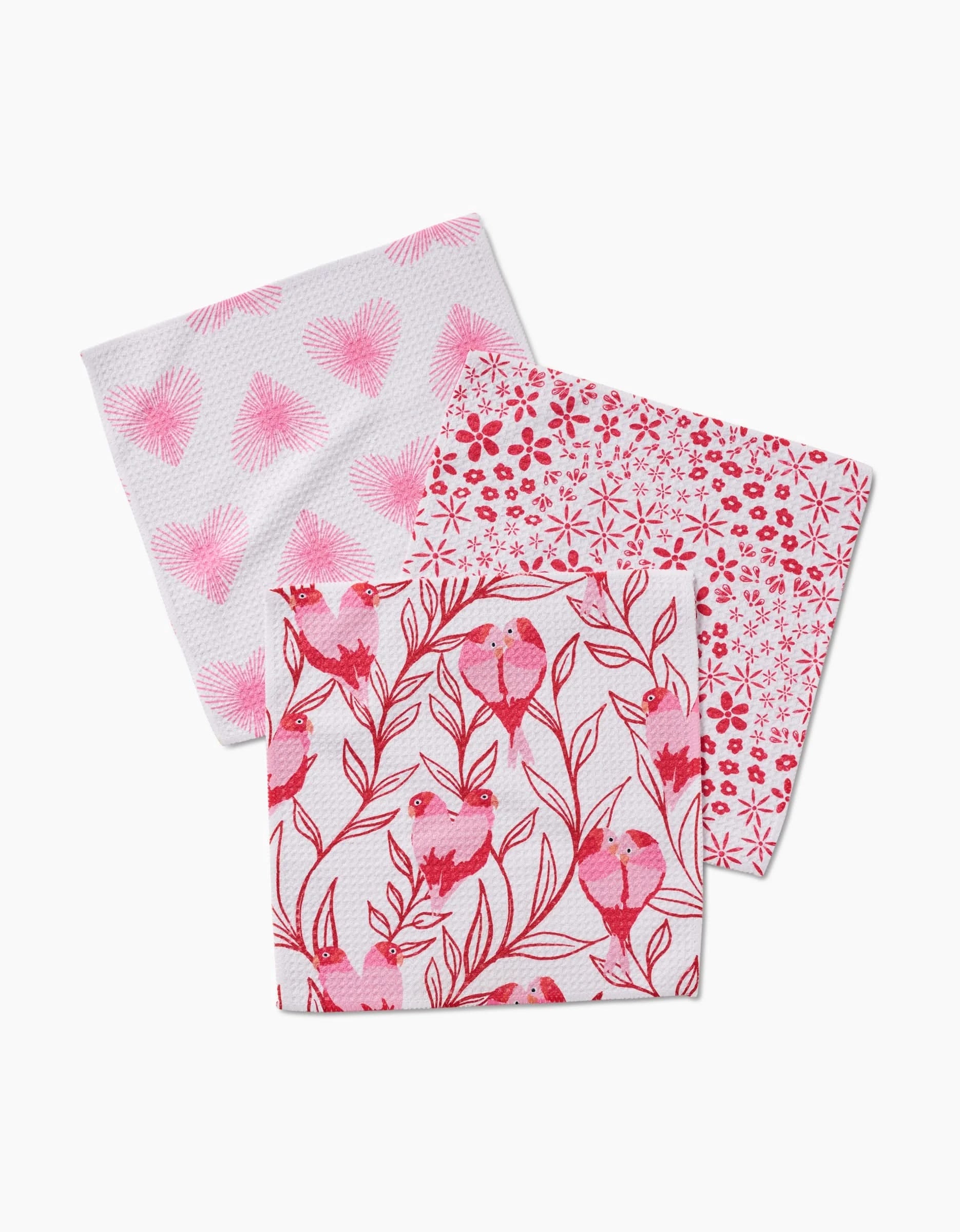 The Love Birds napkin set by Hufton Studio includes three square napkins made from recycled materials, each with a pink-and-white design: hearts, small flowers, and birds on branches.