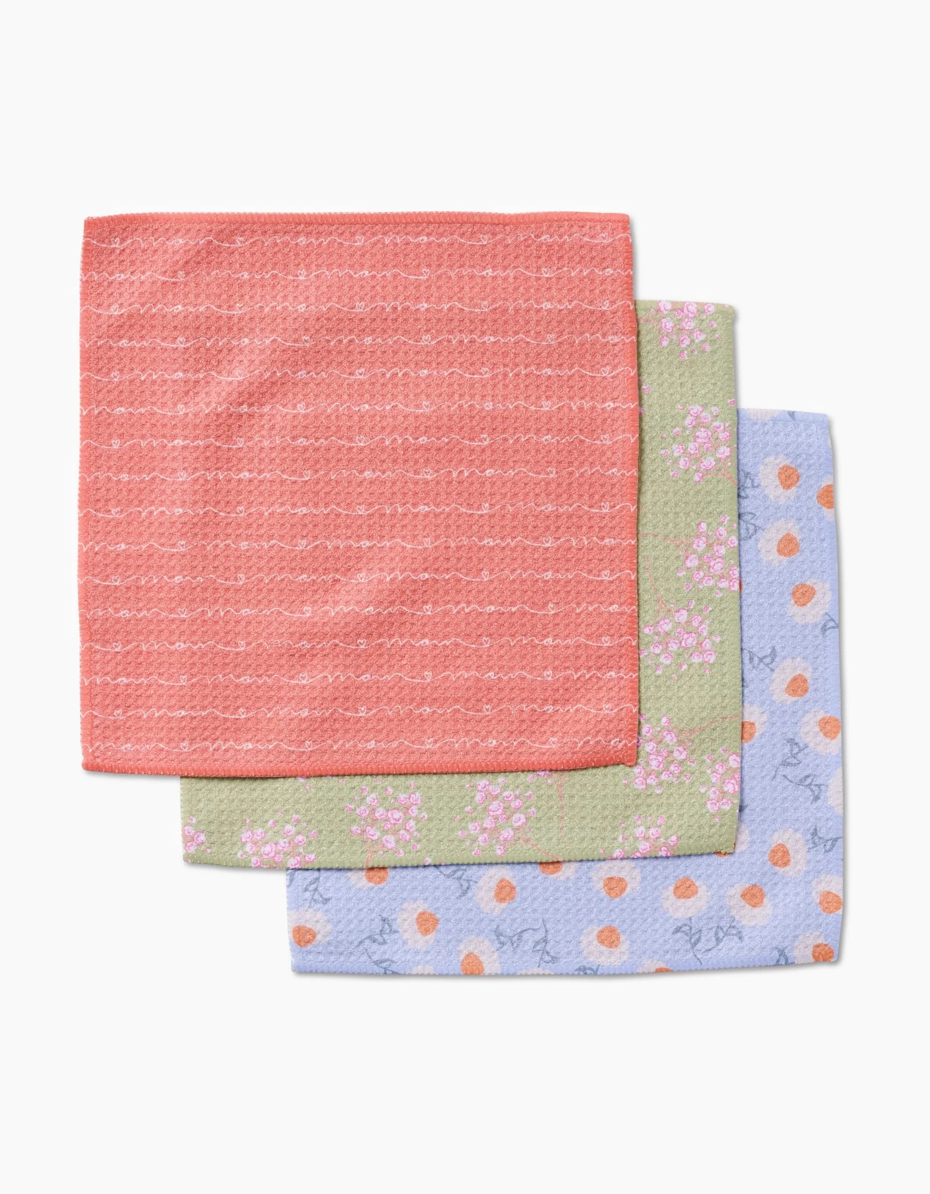 Three “Love of Mom” washcloths by Sarah Reed are stacked: coral with white dashes, light green with pink florals, and light blue with orange dots—each made from durable Geoweave fabric.