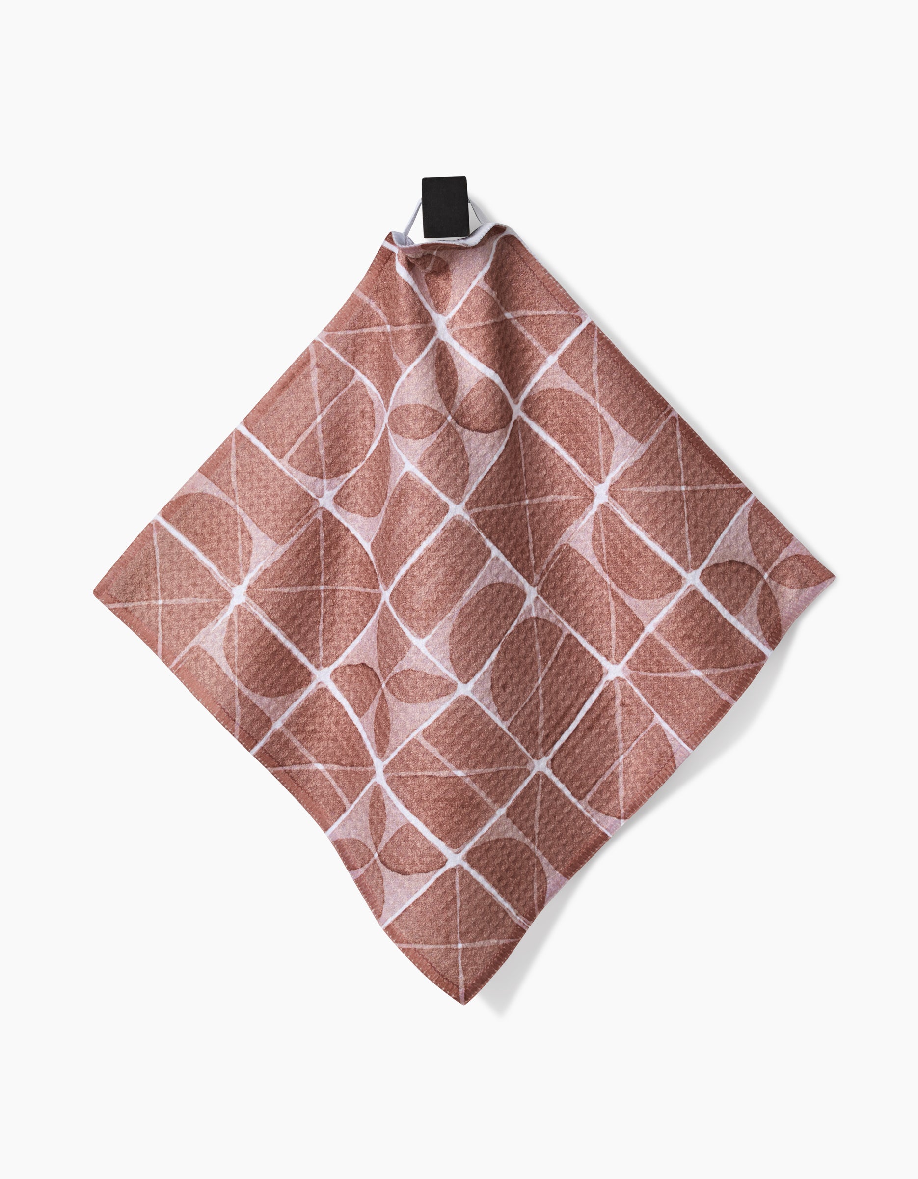 A Mariposa dishcloth from Studio Jeannot hangs by a black loop against a white background, showcasing its pinkish-brown Geoweave fabric with intersecting white geometric lines.