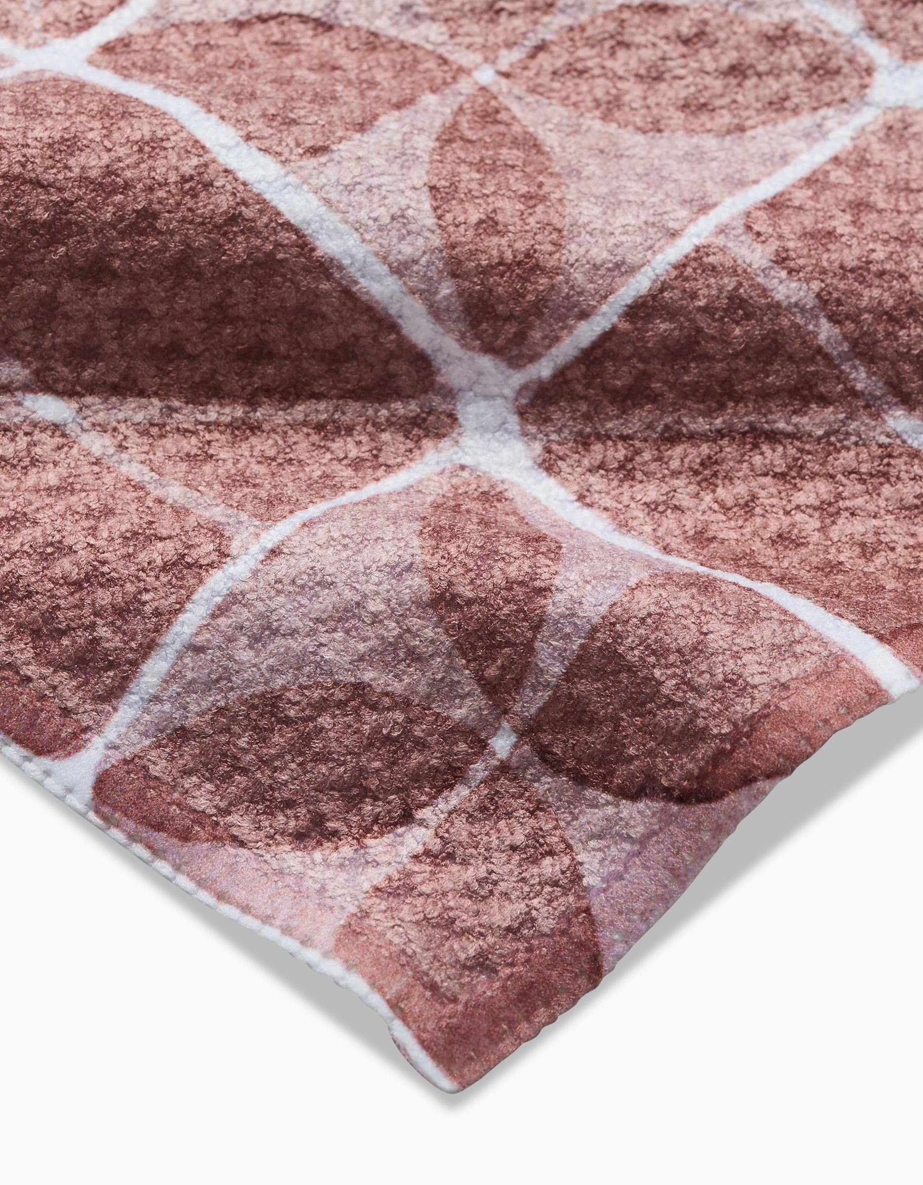 A close-up of Mariposa by Studio Jeannot reveals its Geoweave fabric featuring a geometric pattern of overlapping brown shapes and white lines, highlighting the soft, plush surface and visible fibers at the corner.