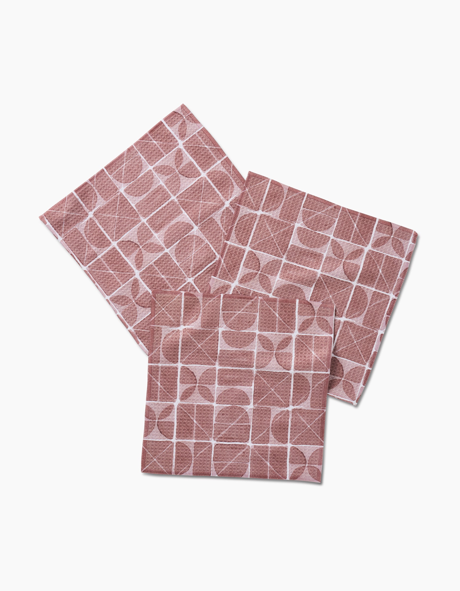 Three Mariposa napkins from Studio Jeannot are made of Geoweave fabric and feature a pink and white geometric pattern with circles and rectangles, shown overlapping on a white background.