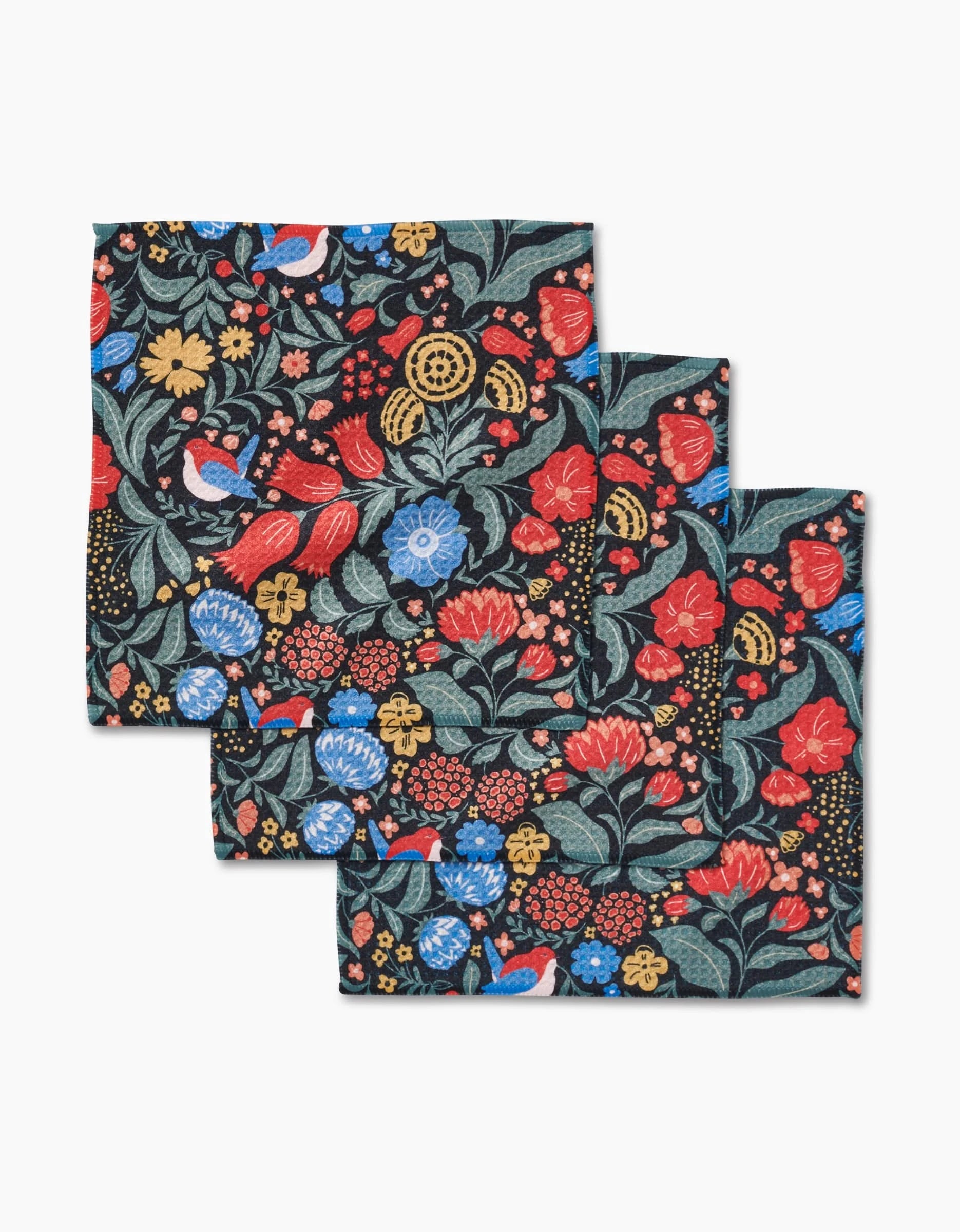 The Marsh Wren napkins by Danelys Sidron are absorbent, eco-friendly fabric napkins featuring a vibrant floral pattern with red, blue, yellow, and green accents, shown stacked against a dark background.