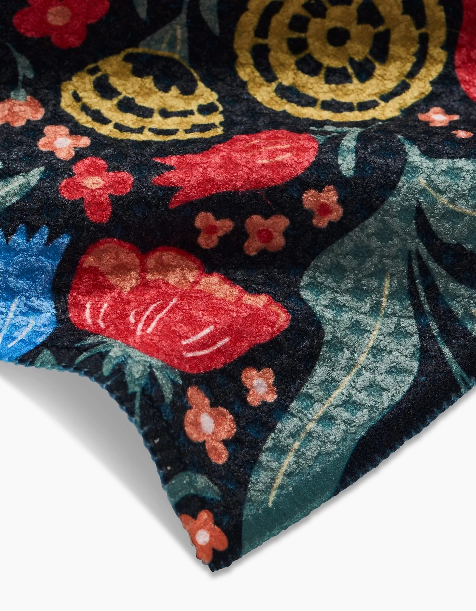 A close-up of the Danelys Sidron Marsh Wren dishcloth, made from recycled materials, features a colorful floral pattern with red, blue, and yellow flowers plus green leaves on a dark background. The absorbent fabric is slightly folded at the edge.