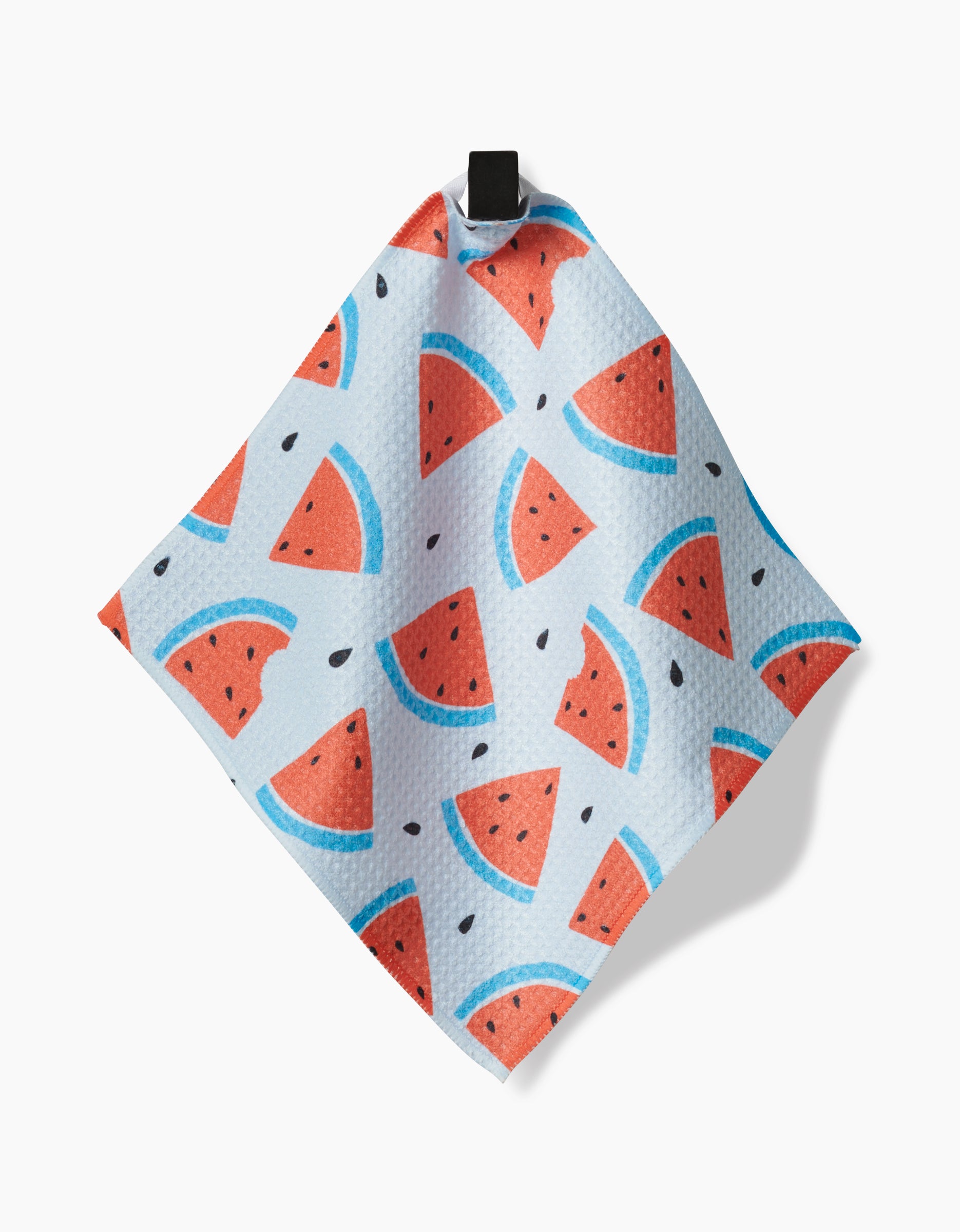 The Sara Mari Melon Mingle dishcloth is a square, eco-friendly kitchen cloth featuring a vibrant watermelon slice design in red, blue, and black on a light background, hanging by its black loop against a plain white surface.