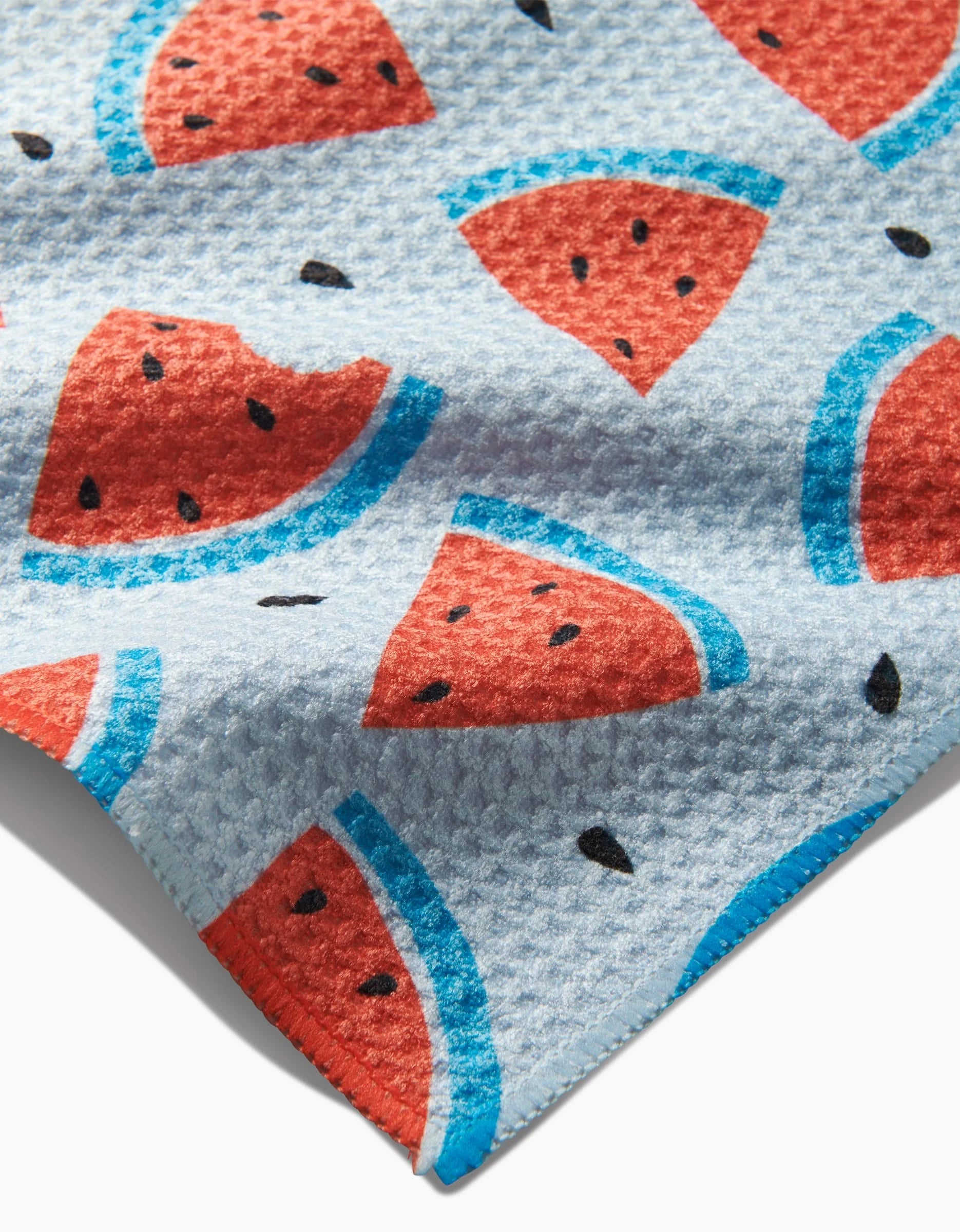 A close-up of Melon Mingle by Sara Mari shows textured Geoweave fabric with red watermelon slices, blue rinds, and black seeds on a light blue background—ideal for stylish, durable dishcloths.