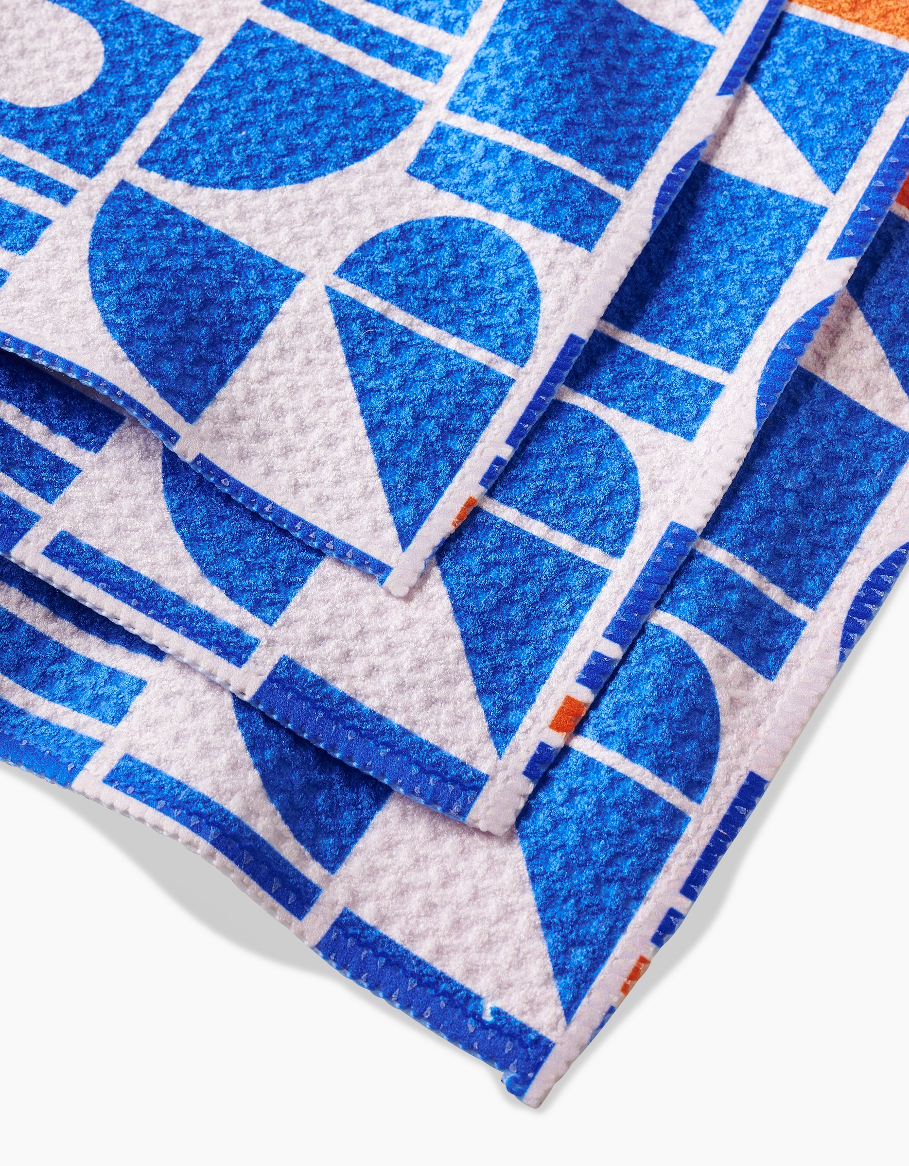 A close-up of Happy Hemeras Misty Oasis shows the textured Geoweave fabric neatly folded, featuring bold blue and white geometric patterns—semicircles, rectangles, lines—and small orange accents.