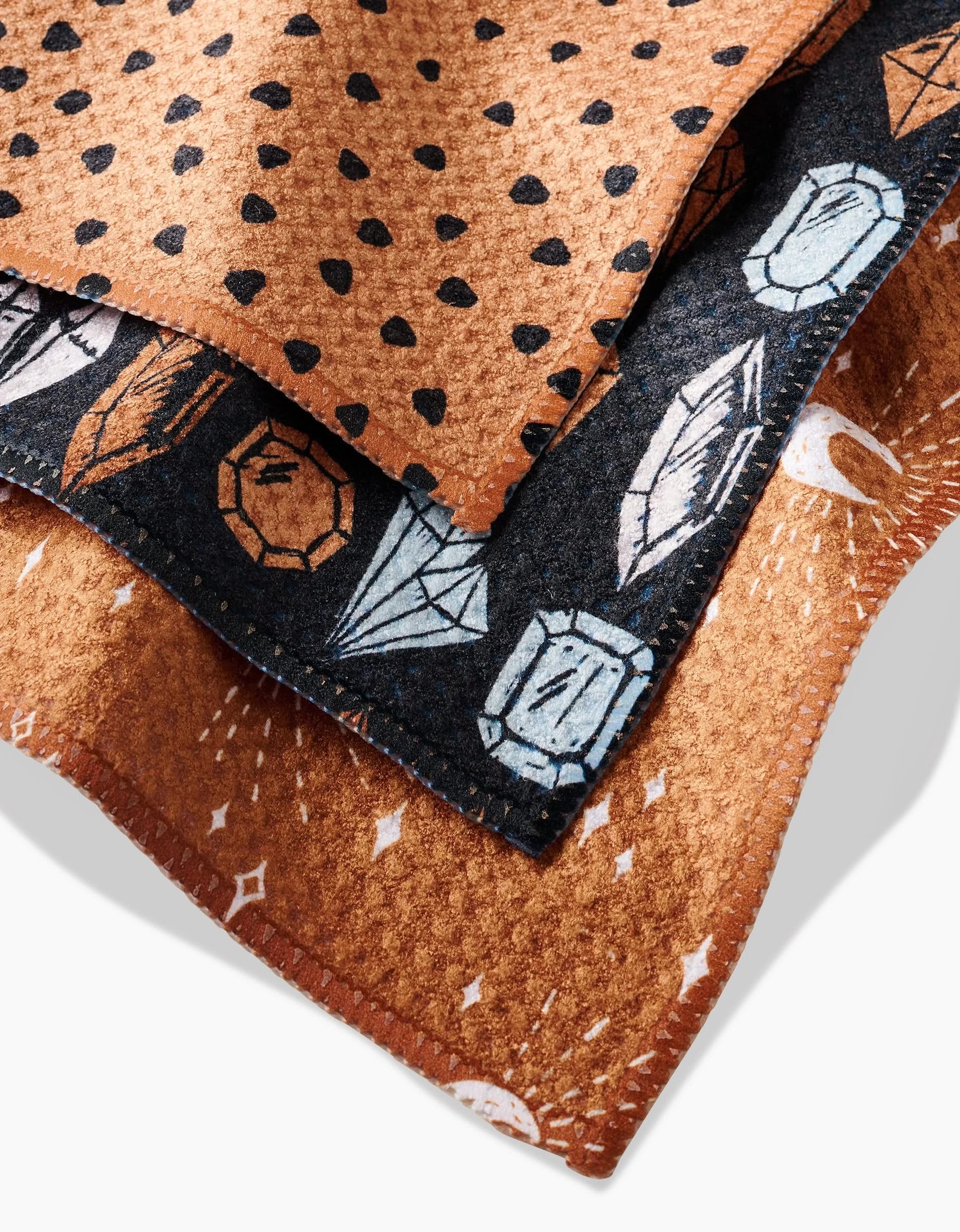 The Moon Craft dishcloth set by Hufton Studio features three eco-friendly Geoweave cloths in brown with black dots, black with gemstones and feathers, and brown with white celestial designs, all soft and slightly textured.