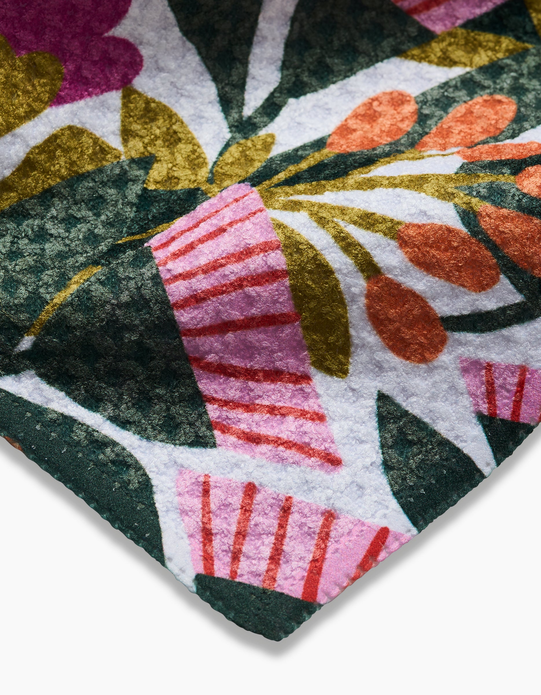 Close-up of Lisa Nelsons Moxie Mauve Geoweave dishcloth, featuring a colorful abstract floral pattern in green, pink, red, orange, and white on textured fabric, with the edge of the material shown against a white background.