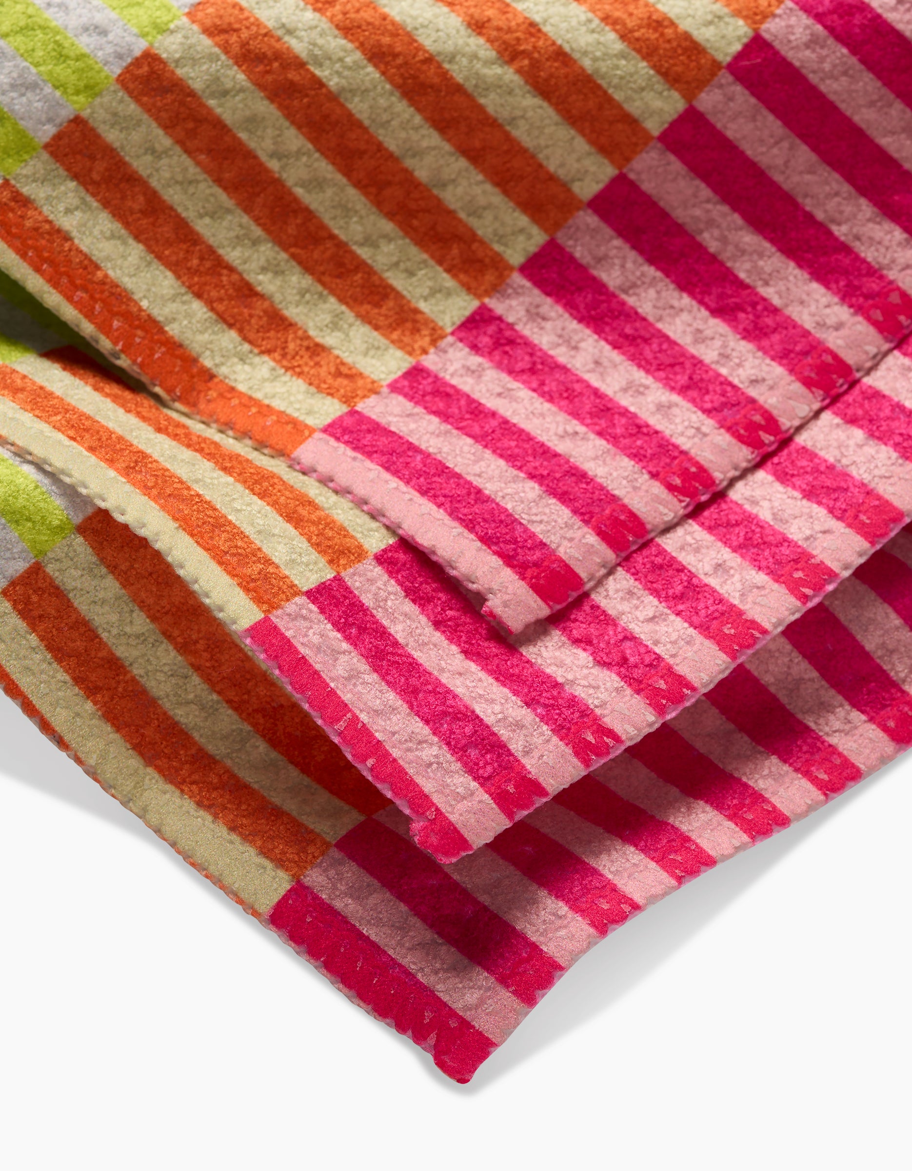 A close-up of the GEOMETRY Neon Nights dishcloth, featuring folded geoweave fabric with colorful pink, orange, green, and beige stripes and visible edge stitching.