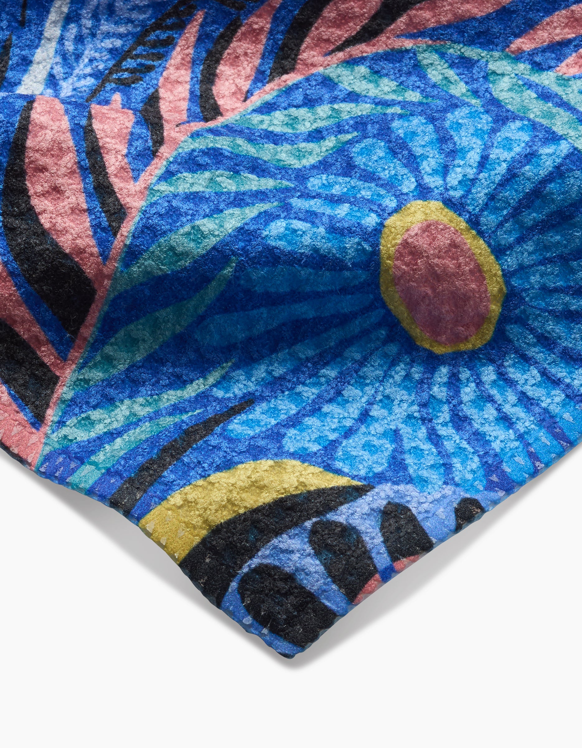 A close-up of the Palm Beach dishcloth by Masha Volnova, showcasing a vibrant abstract design with blue swirls, a red and yellow center, and black, pink, and yellow accents on textured Geoweave fabric.