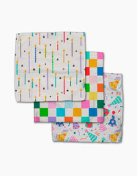 Three colorful Party Pop Geoweave cloths by Vaishali Design Studio are stacked: the top has birthday candles, the middle a multicolored check pattern, and the bottom shows party hats, cupcakes, and confetti on an eco-friendly white background.