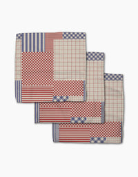 The Geometry Patched Up Parade set includes three folded cloth napkins made from recycled materials, featuring red and blue patchwork patterns—checks, stripes, and grid designs on white.