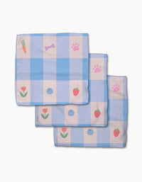 Pawfect Picnic by Letters By Shells: Three folded blue and white checkered dishcloths made from recycled materials feature cartoon prints—carrot, bone, paw print, flower, strawberry, and blue dot—stacked on a white background.