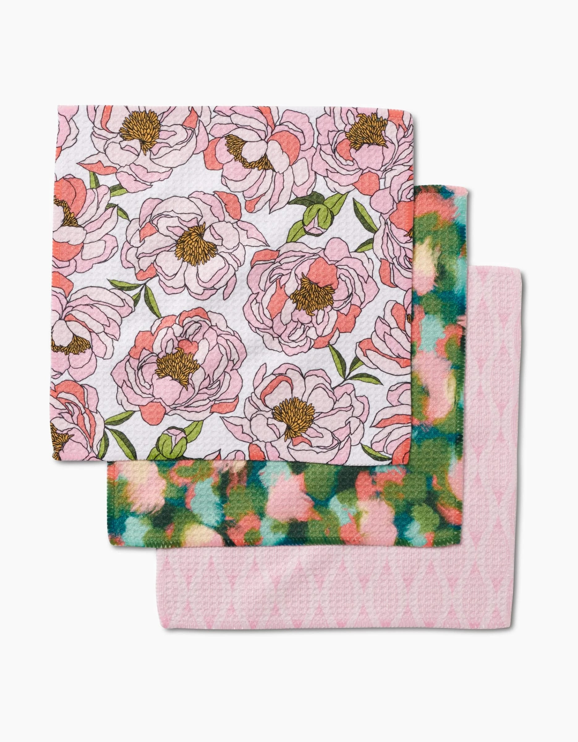 Two colorful Shelley Smith dishcloths are stacked: the top, Peony Paradise, displays a pink floral pattern with green leaves on Geoweave fabric; the bottom shows green, blue, and pink hues over a pale pink patterned cloth.
