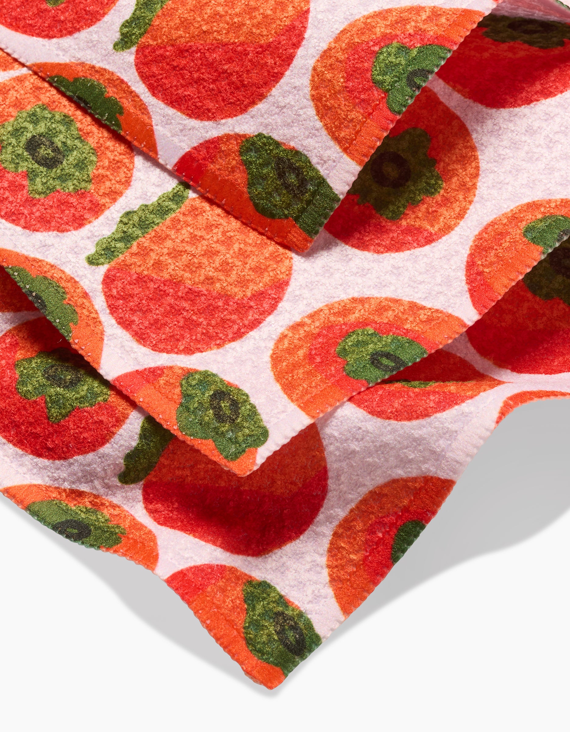 A close-up of the Persimmons Geoweave dishcloth set by Katie OShea, showcasing a bright orange persimmon pattern with green tops on a white background.