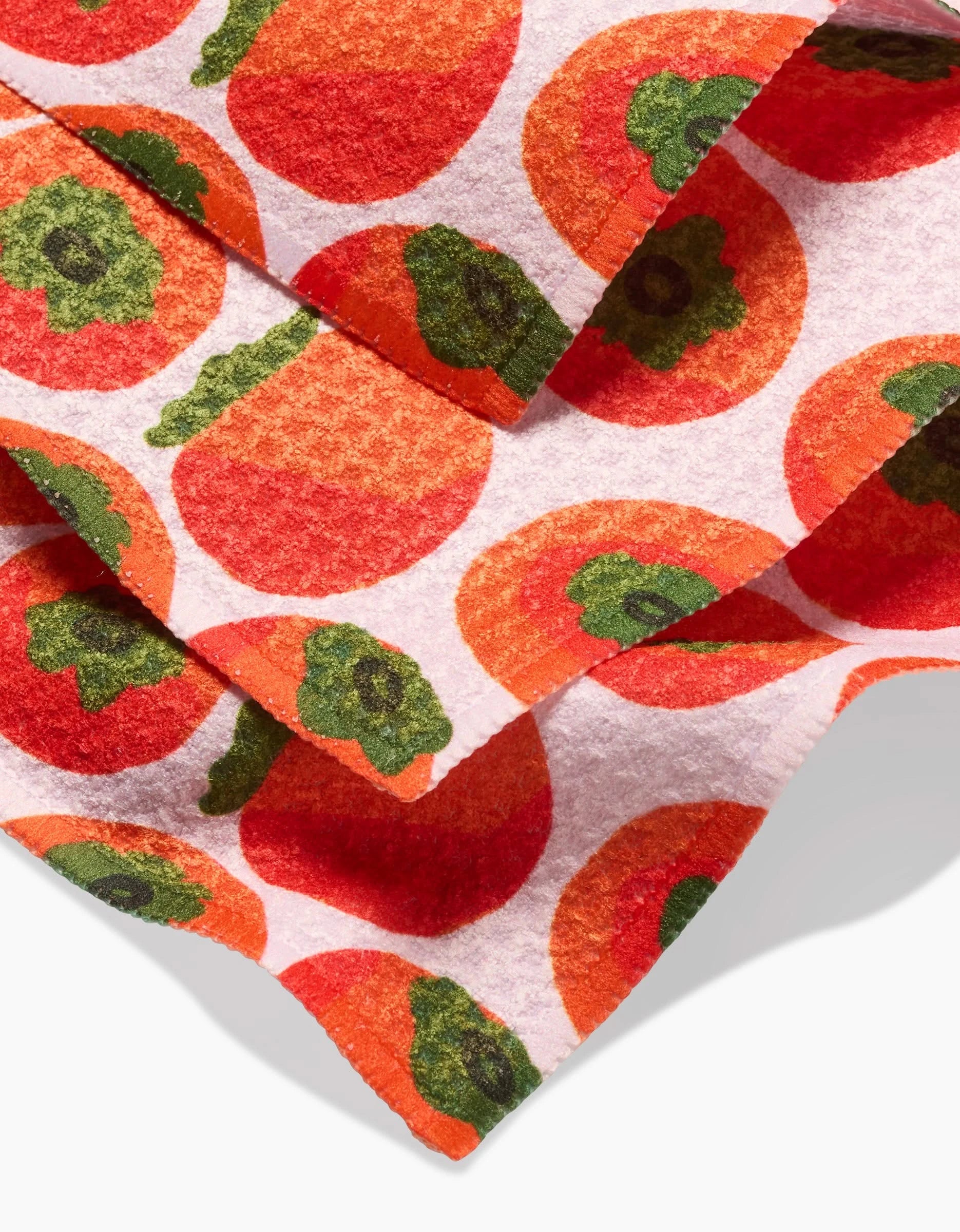A close-up of the Persimmons Geoweave dishcloth set by Katie OShea, showcasing a bright orange persimmon pattern with green tops on a white background.