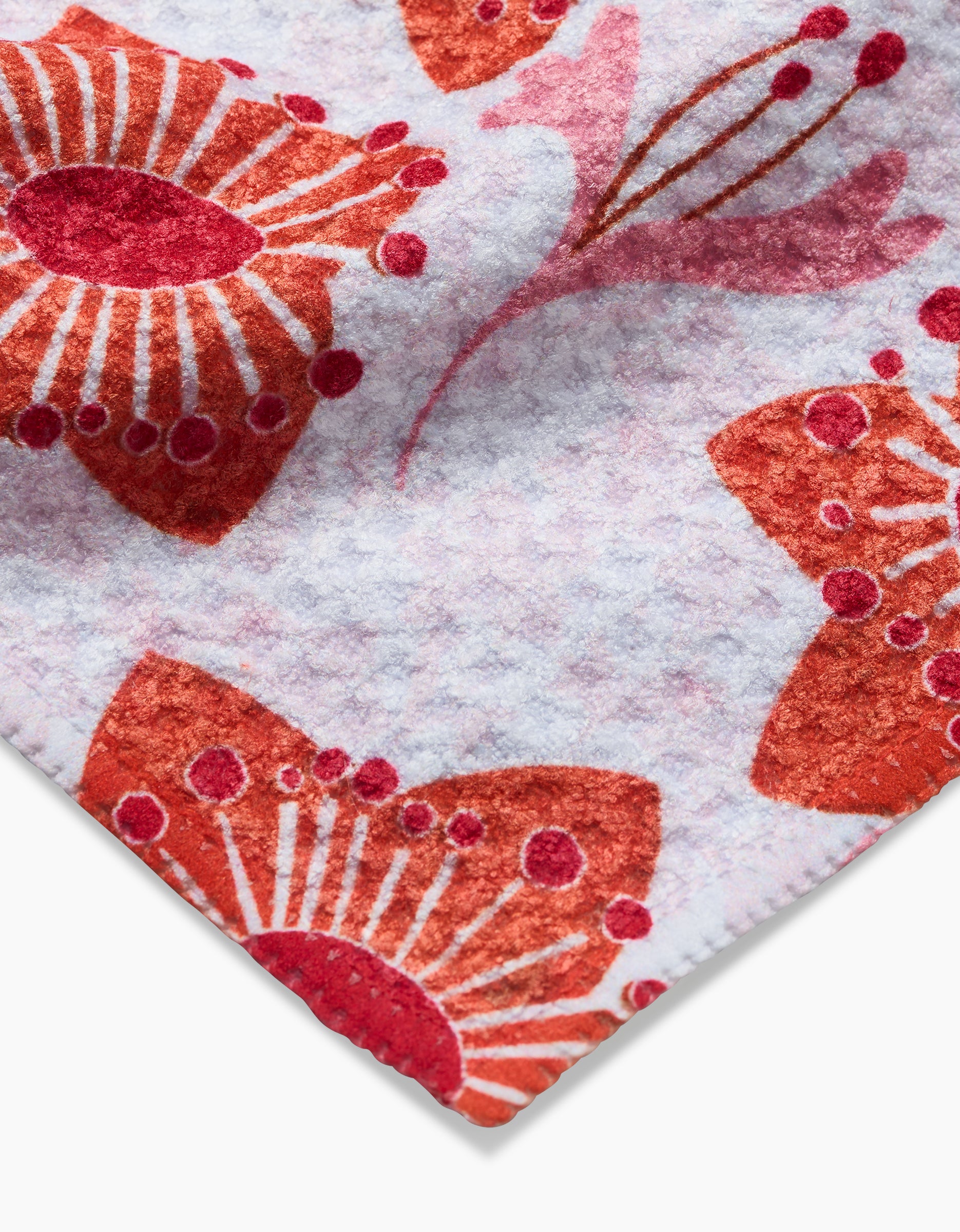 Close-up of Whitney Urquhart’s Petal Paradise dishcloth, crafted from soft white Geoweave fabric and adorned with a red and orange abstract floral pattern.