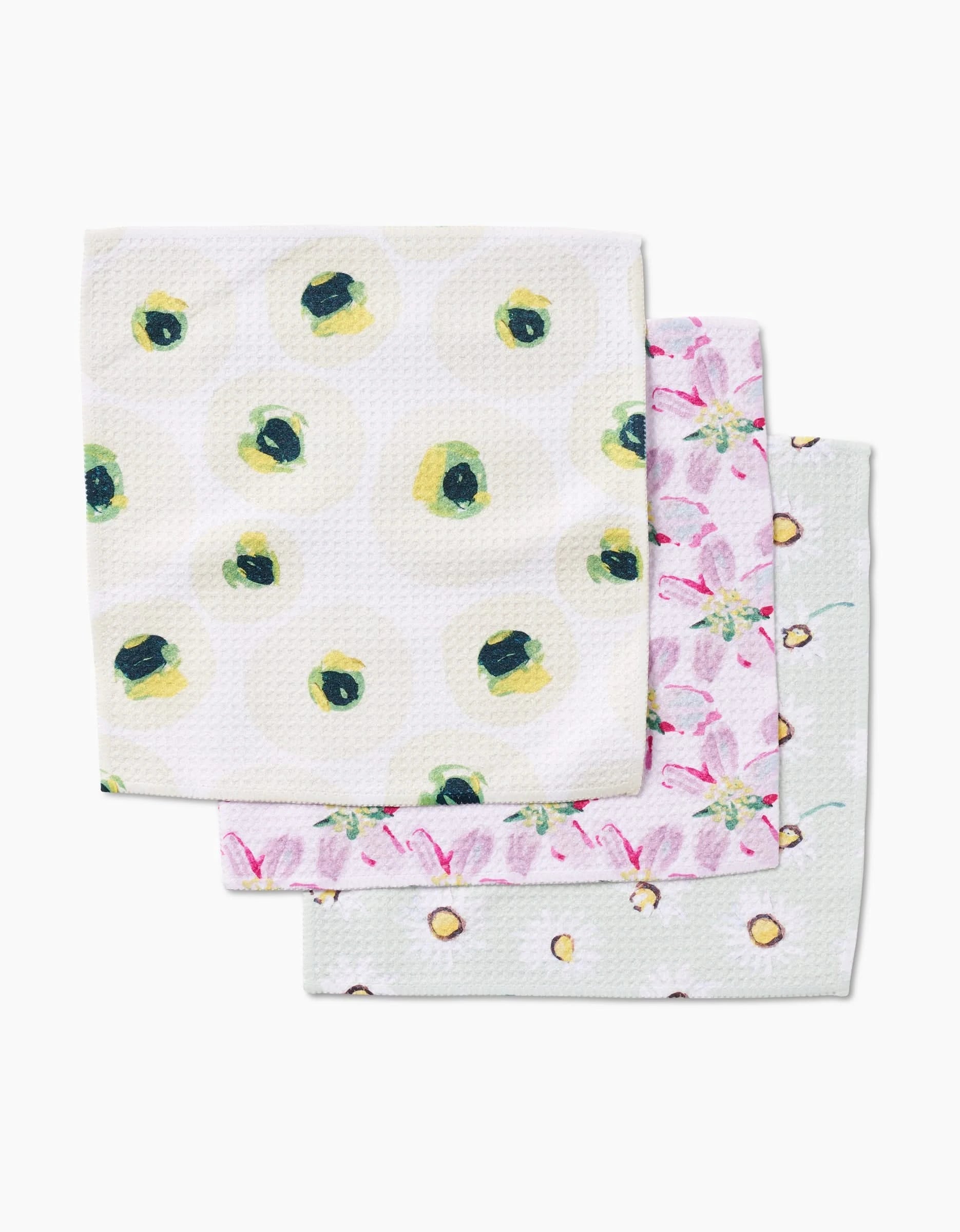 Three patterned cloth napkins by Ania Zwara Art, from the Petals collection, are stacked. Crafted from Geoweave fabric, they feature green olive, pink floral, and yellow dotted circle designs.