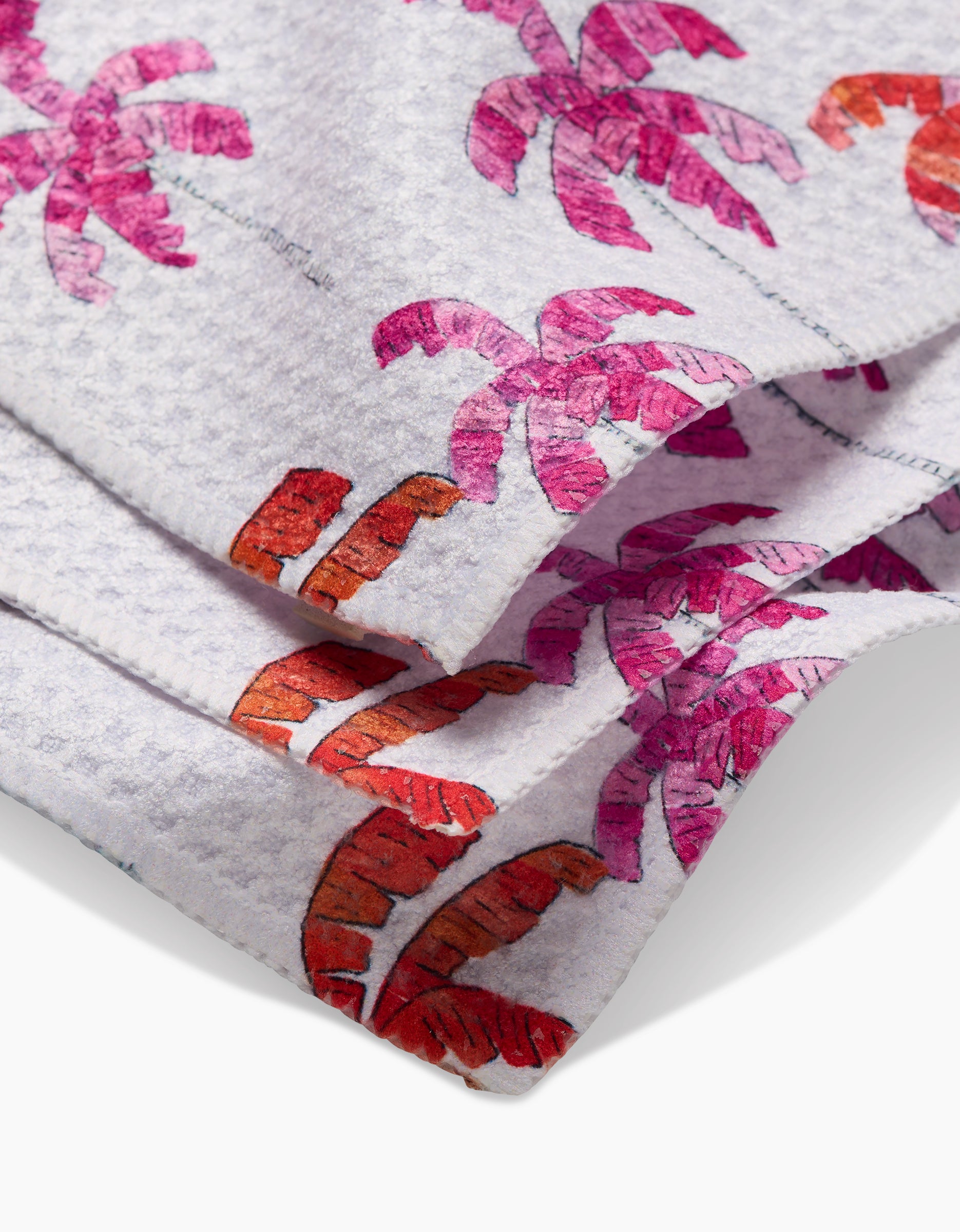 Close-up of the GEOMETRY Pink Palms towel, featuring a folded white design with textured Geoweave fabric and a vibrant pink and orange palm tree pattern.