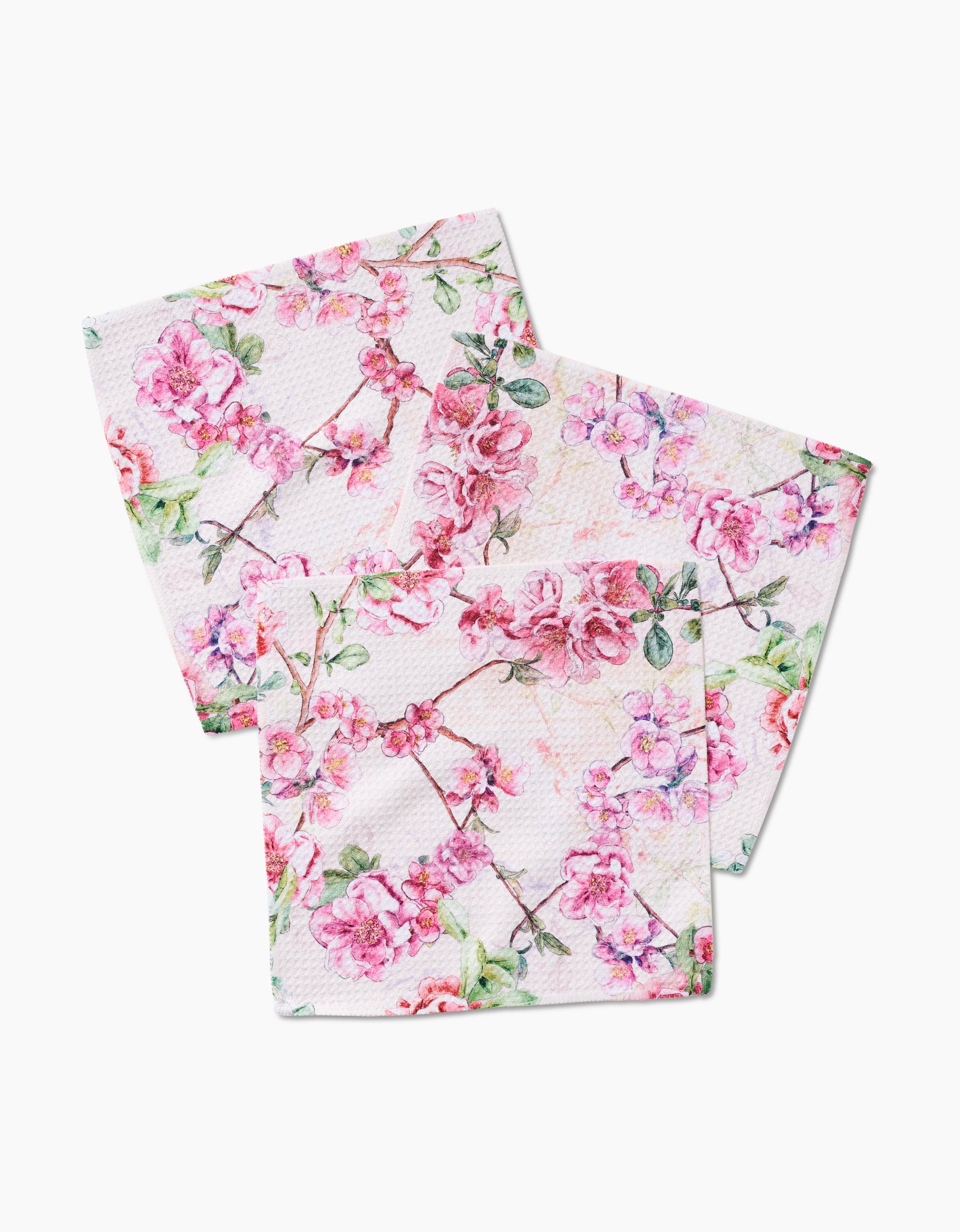 Two square Primroses cloth napkins by Pascale Dilger, made of Geoweave fabric, feature overlapping pink floral branches with green leaves on a white background.