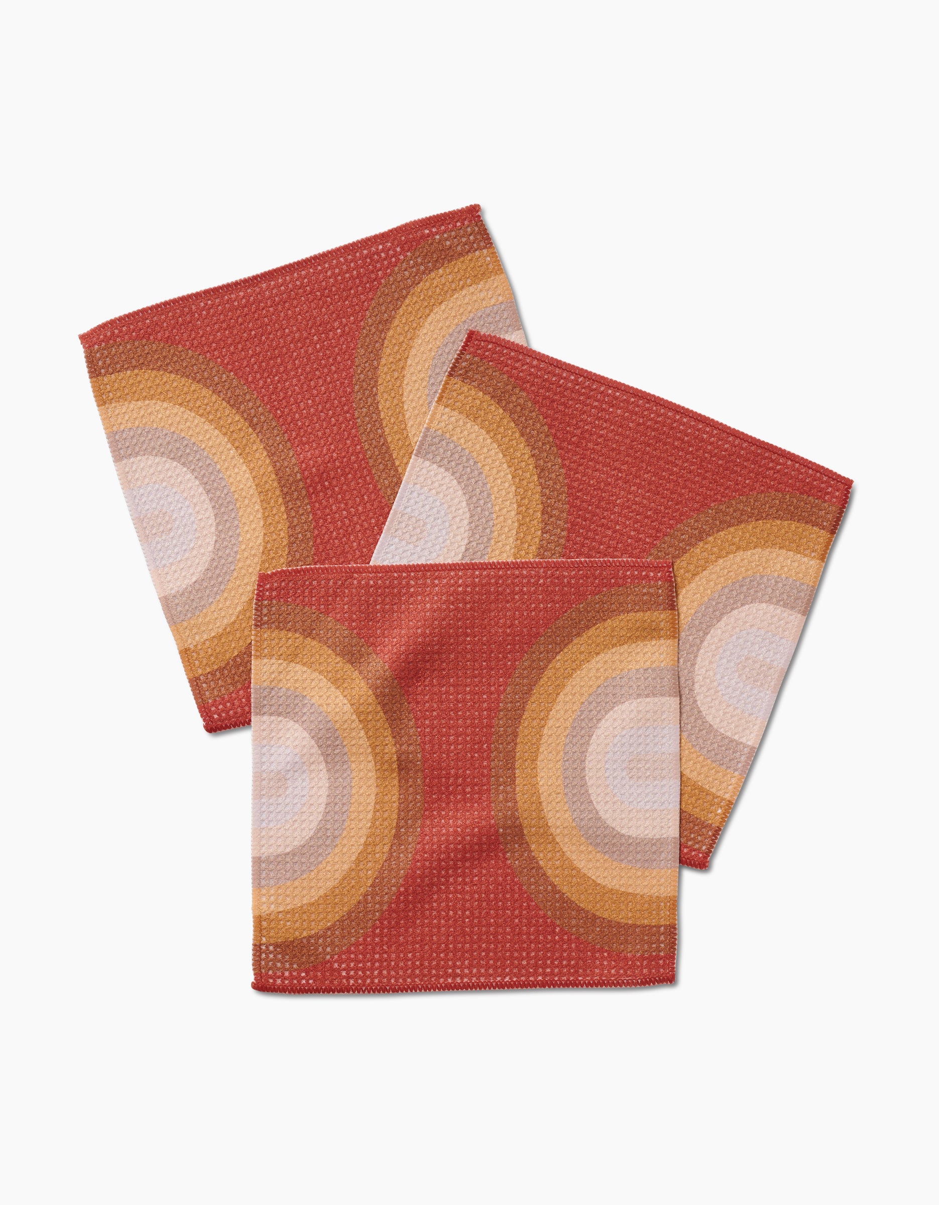 Three square Pumpkin Spice napkins by GEOMETRY, made from recycled materials, feature a retro circular orange, yellow, and white pattern on red, overlapping on a white surface.