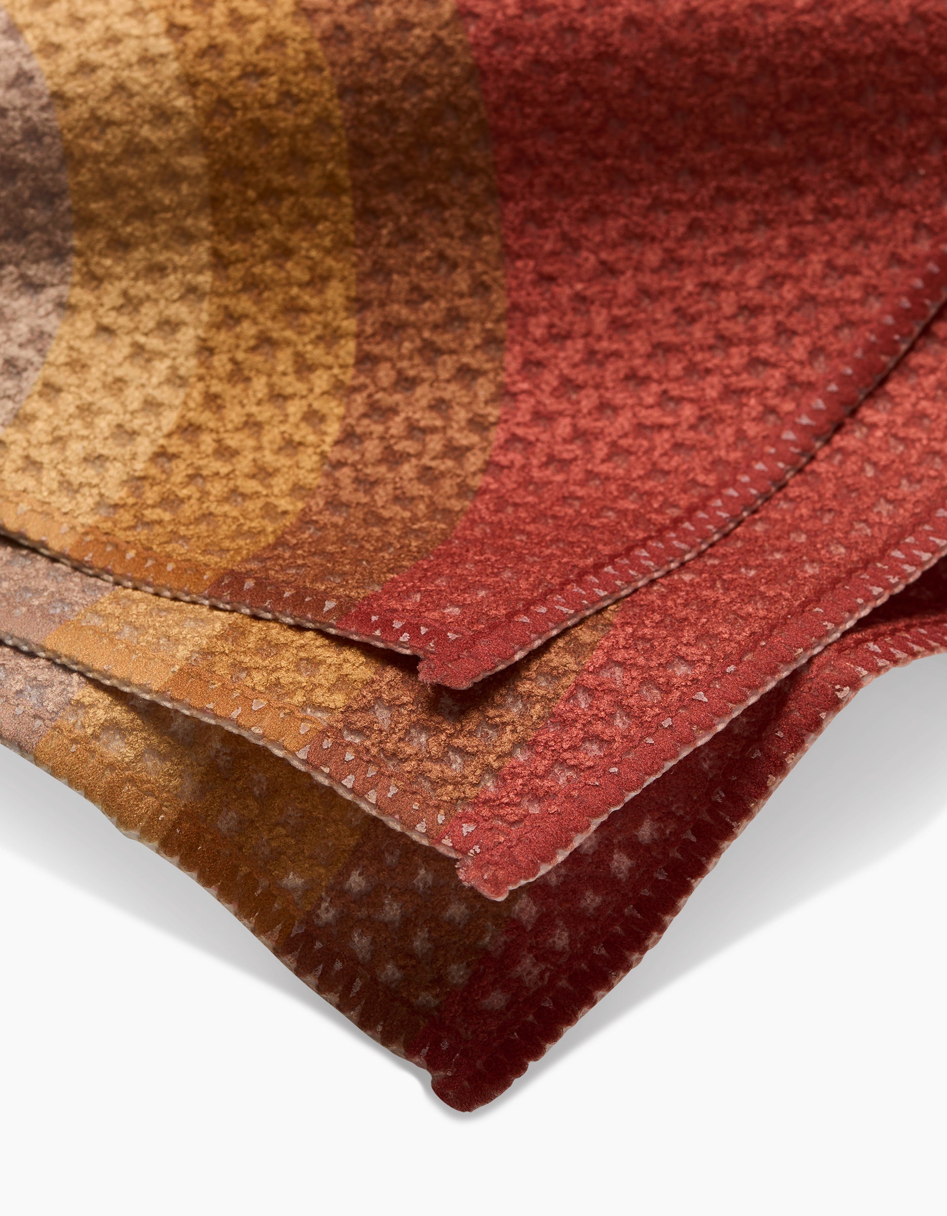 A close-up of GEOMETRY’s Pumpkin Spice Geoweave fabric swatches in warm red, orange, gold, and brown tones with a small geometric pattern and neatly cut edges.