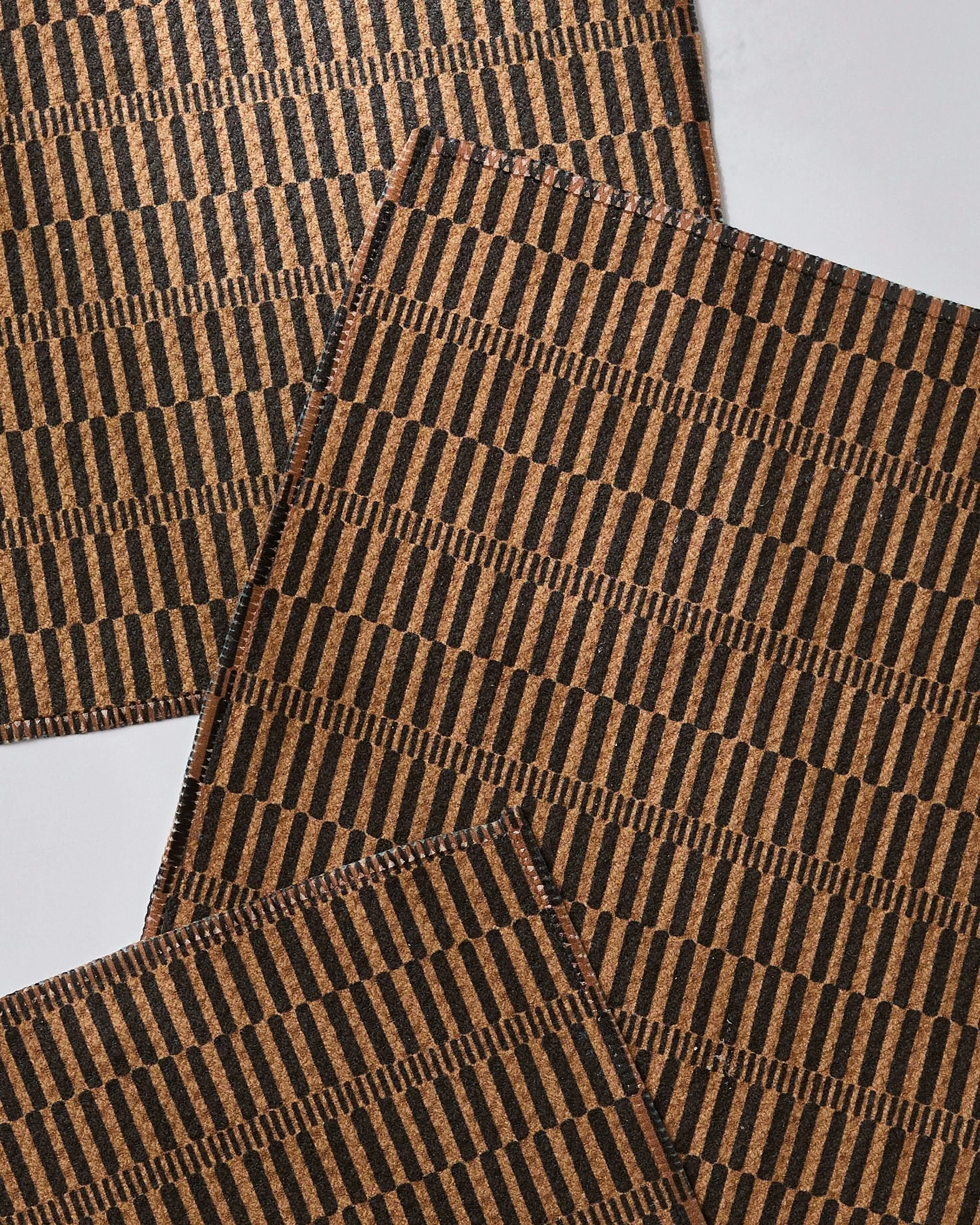 Four Ridge cork placemats by Geometry, featuring a repeating black geometric vertical line pattern, arranged overlapping on a white surface. Made from recycled materials for an eco-friendly touch.