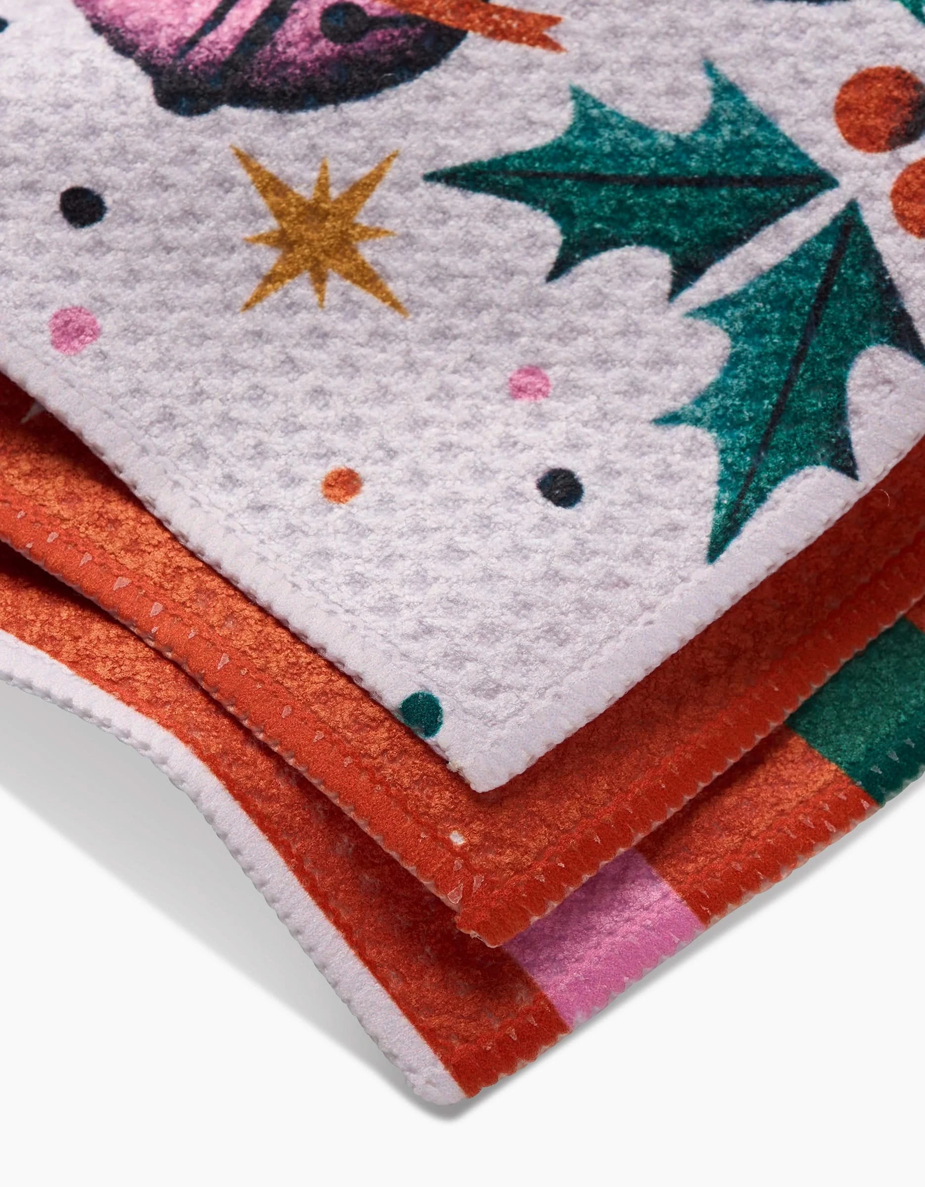 Close-up of three stacked Ring-A-Ling festive dishcloths by Megan Roy, showcasing colorful holiday designs—holly leaves, berries, stars, and polka dots—with Geoweave fabric texture and neatly sewn edges.