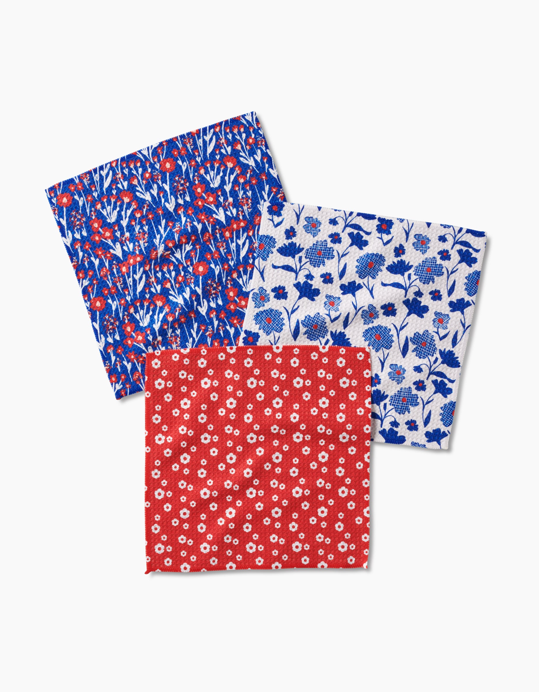 The Royal Garden napkin set by Danelys Sidron includes three recycled cloth napkins with floral patterns: blue and red flowers on dark blue, blue flowers on white, and small white flowers on red.