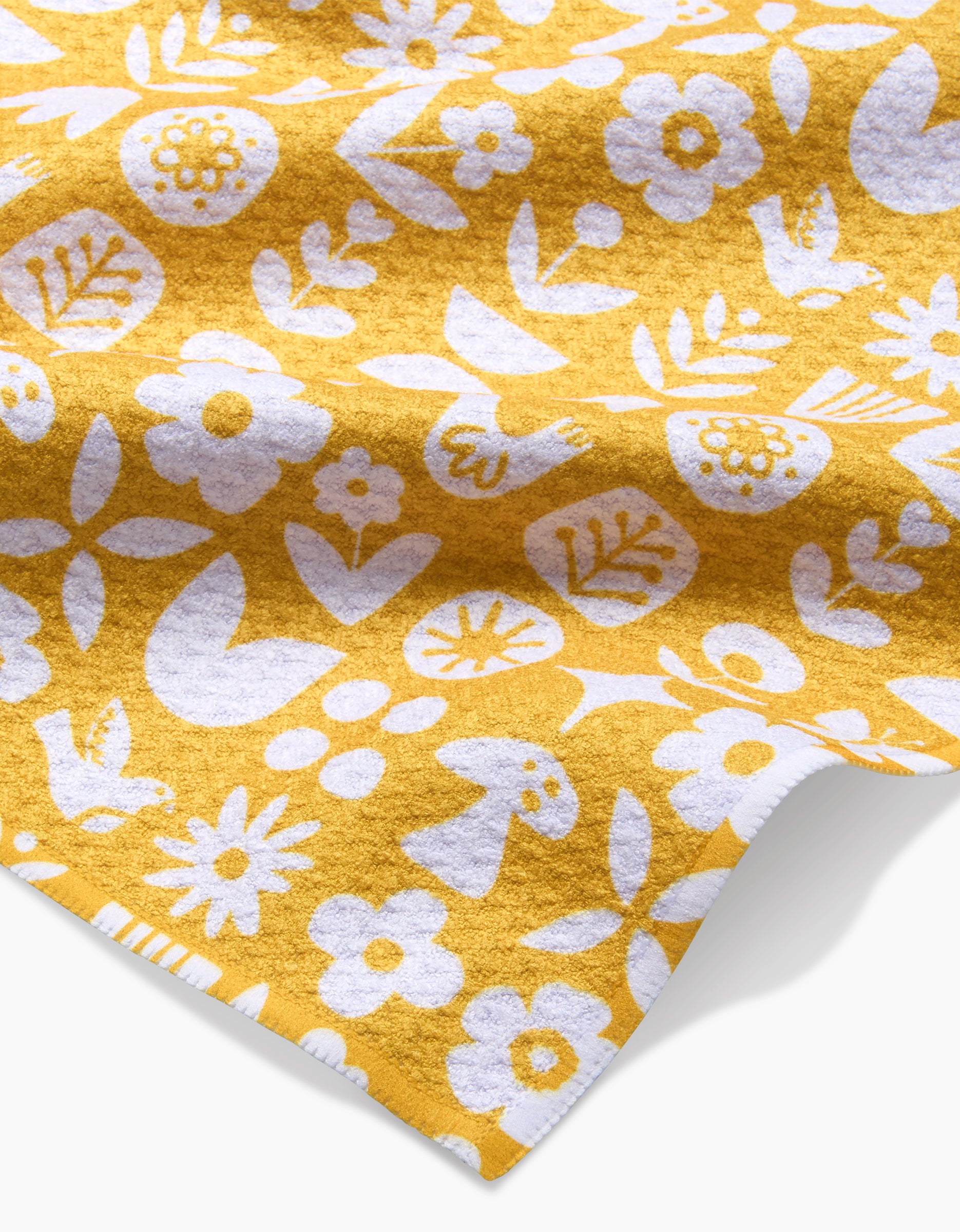 The Kayla Ann Scandi Spring dishcloth features a whimsical white print of flowers, leaves, and mushrooms on yellow Geoweave fabric, with a slightly folded corner highlighting its textured, super-absorbent surface.